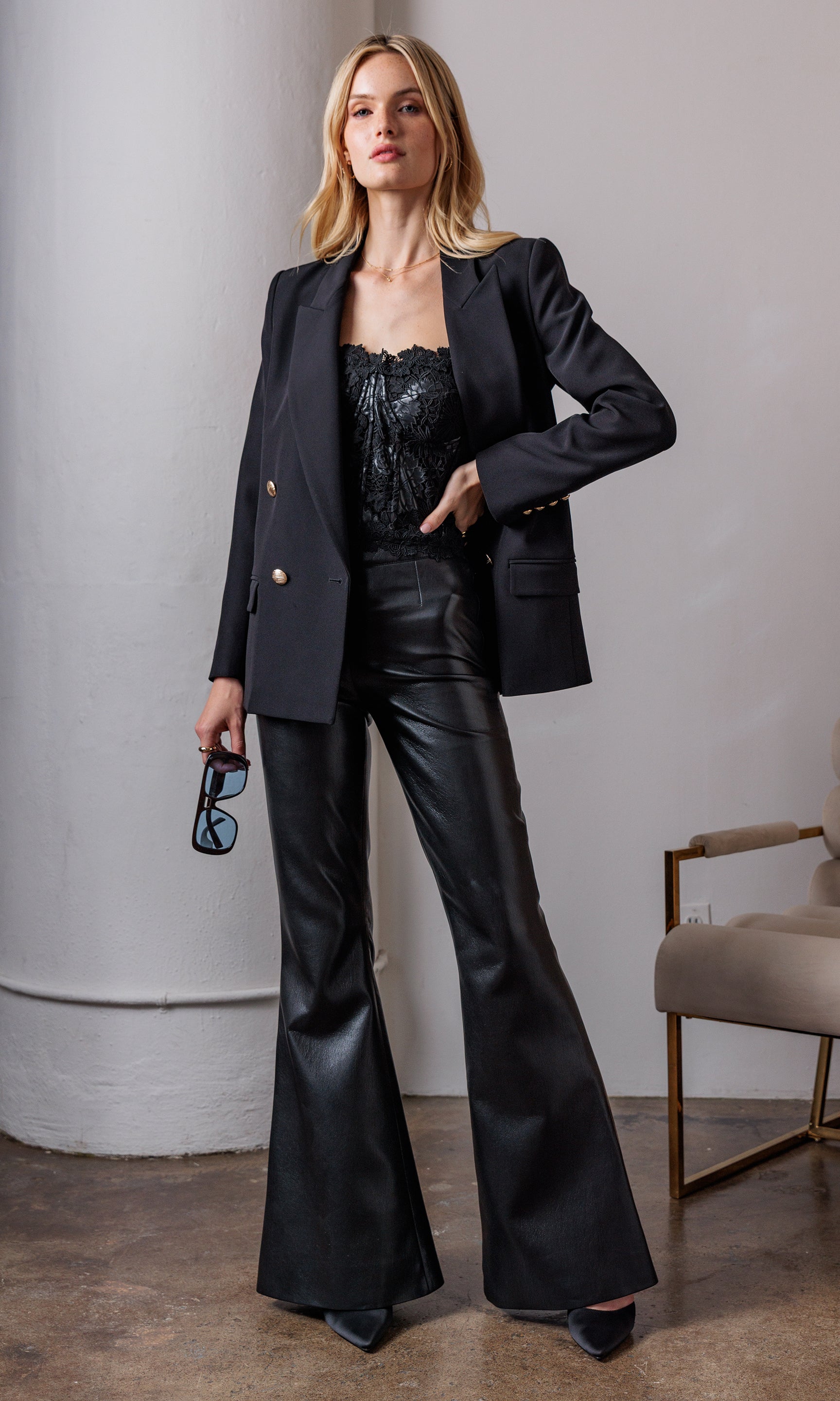 Full body shot of the model in the blazer with leather pants, hands in pockets, exuding a confident stance.