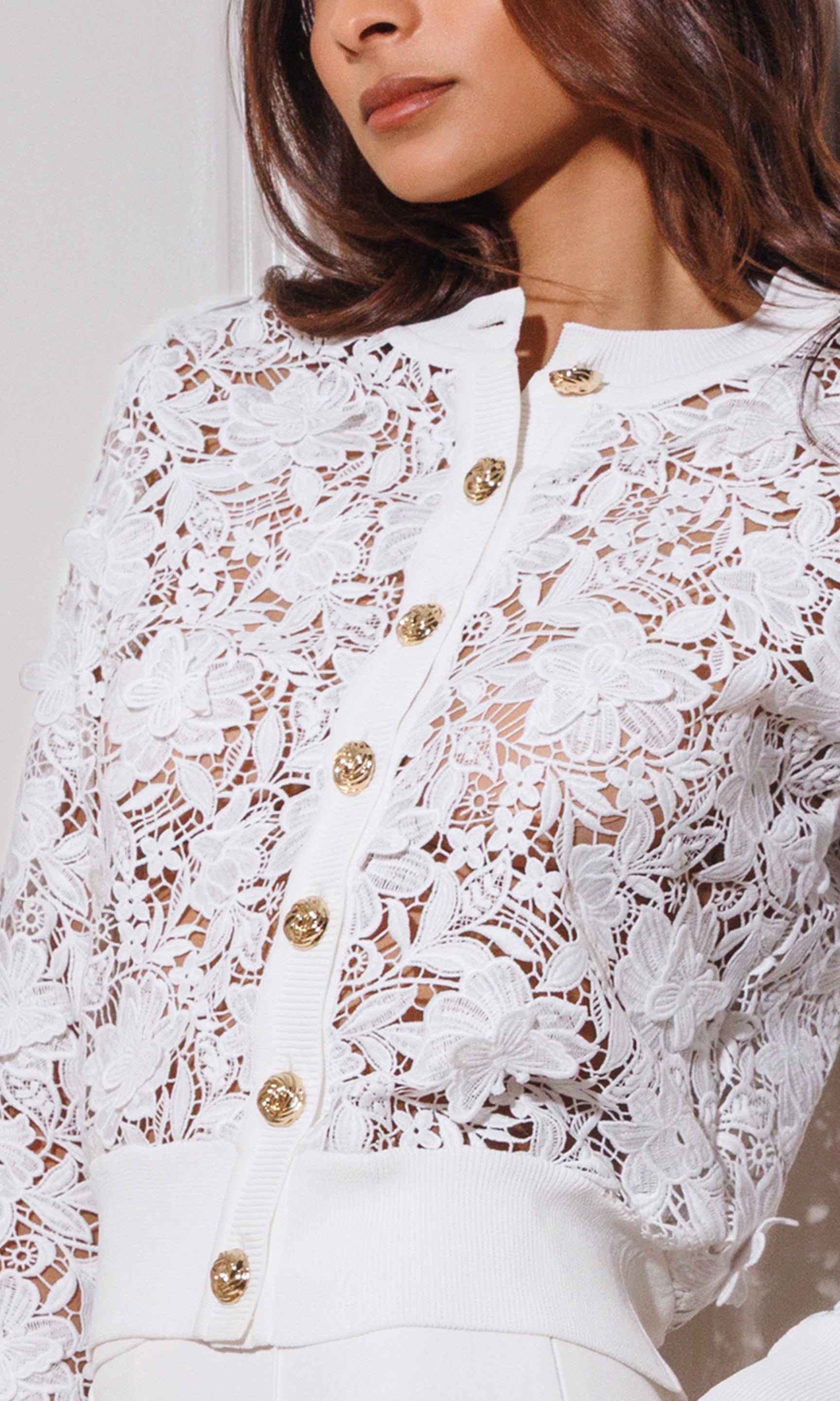 Close-up of white lace cardigan with gold buttons worn by a person.