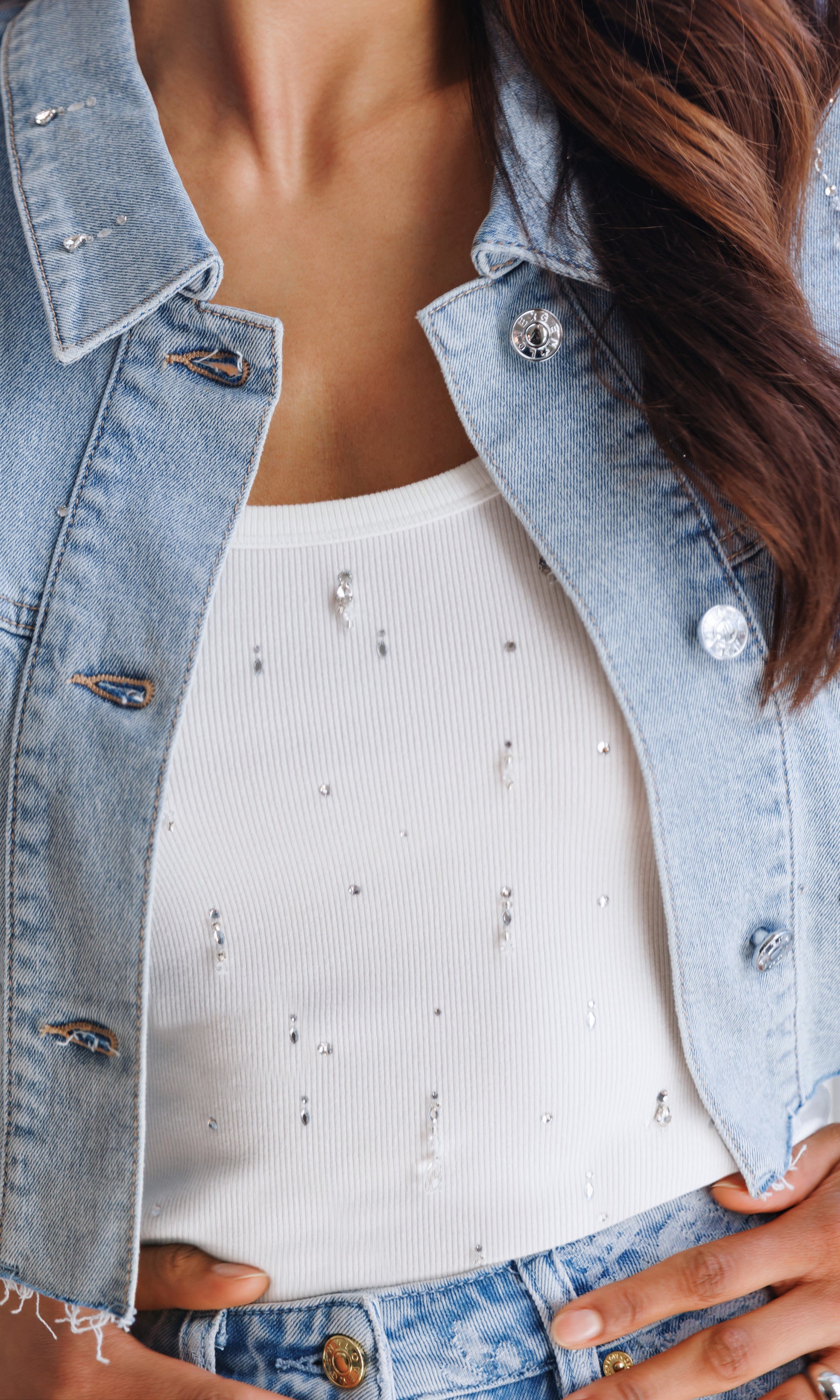 In a close-up front view, the model layers the Evita Embellished Top in white under a denim jacket, focusing on the subtle sparkle and fitted tank silhouette.