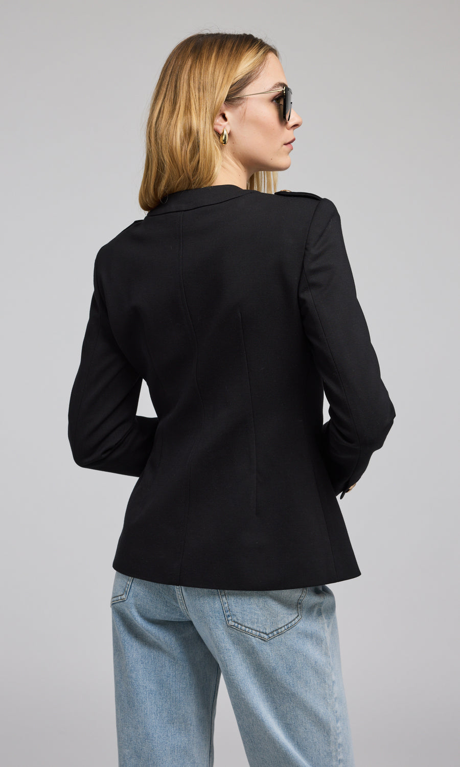 A chic black blazer with buttons is worn by the model, highlighting a refined and fashionable appearance. 