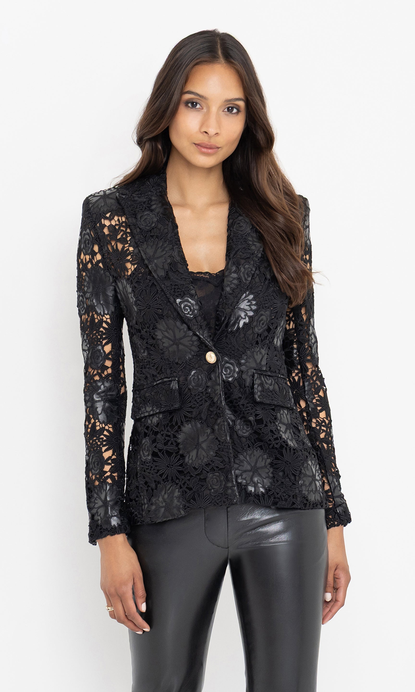 The model poses in a front-facing stance wearing the Aimee Vegan Leather Guipure Blazer, highlighting its intricate floral lace and single-button closure.