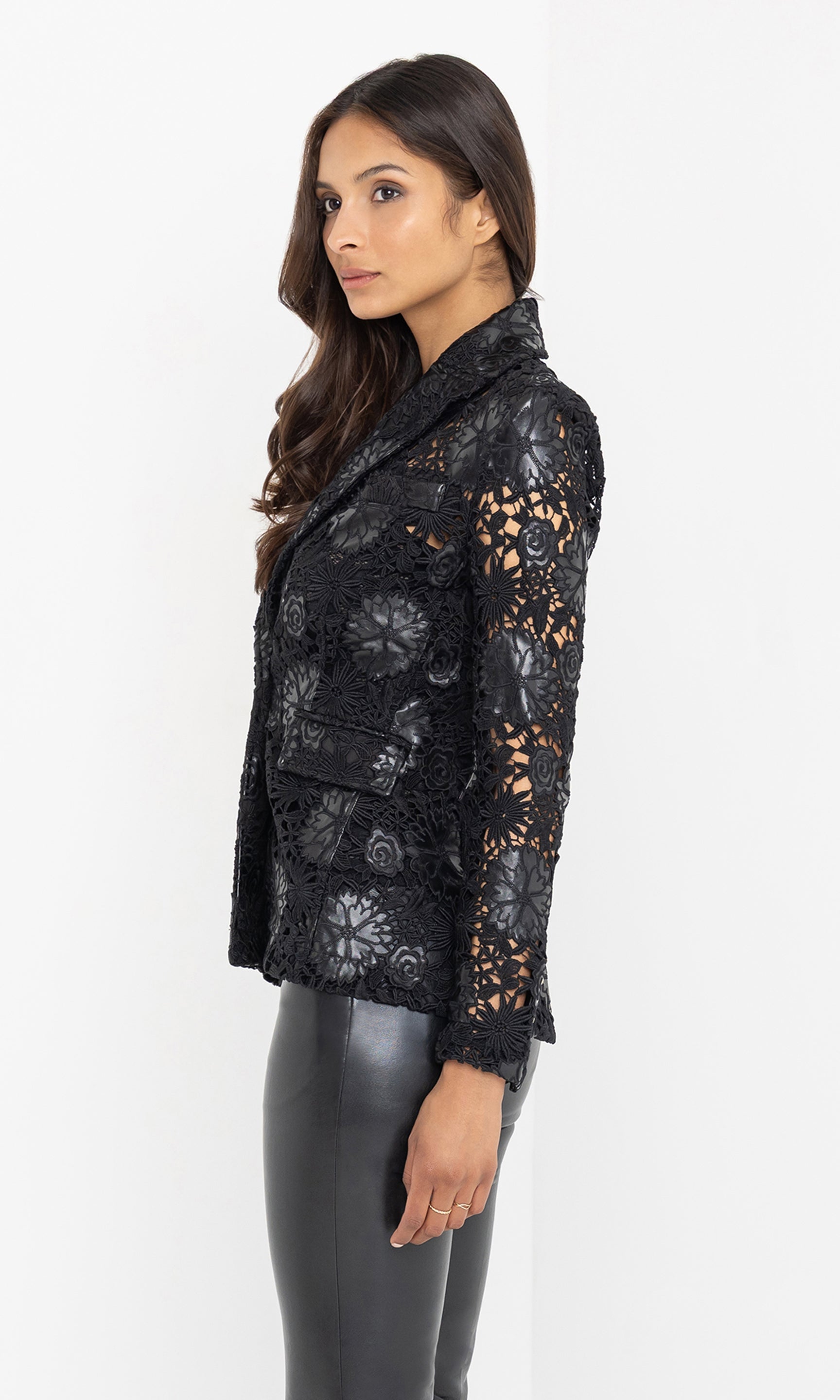 Captured in a side view, the model subtly turns to emphasize the structured shoulders and dimensional lacework of the blazer.
