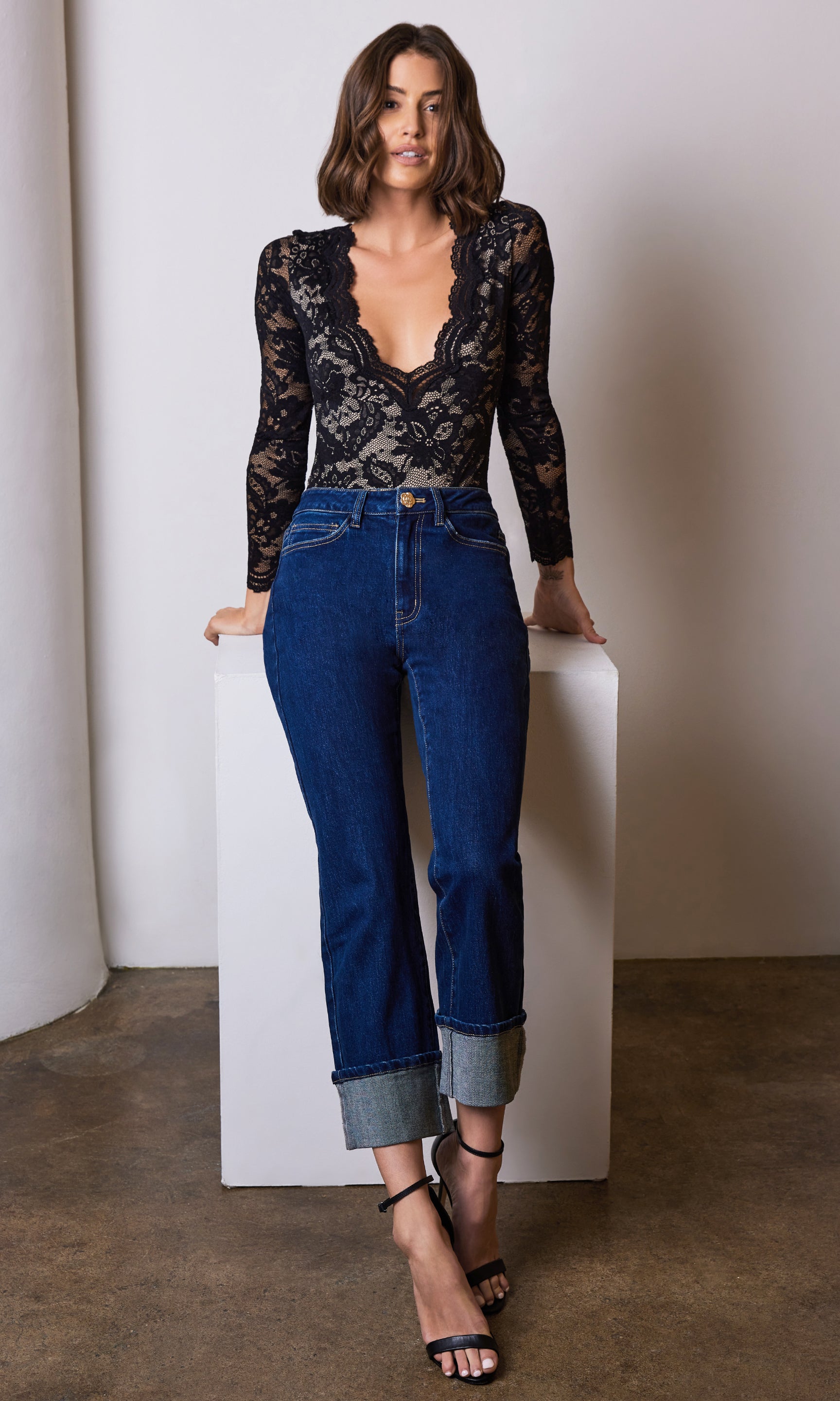 Woman wearing a black lace top and blue jeans against a neutral background