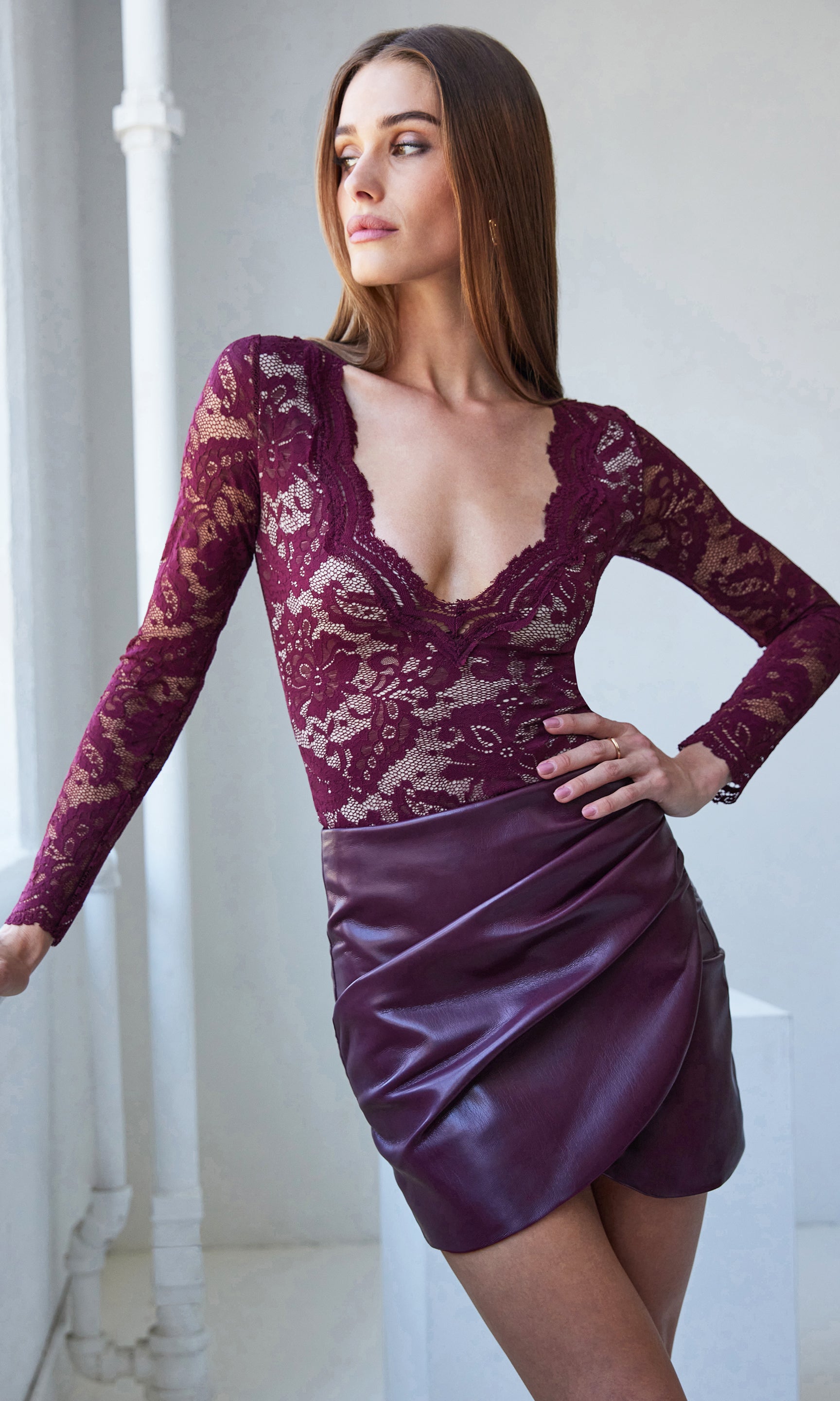 Woman wearing a burgundy lace bodysuit with a burgundy skirt against a white background
