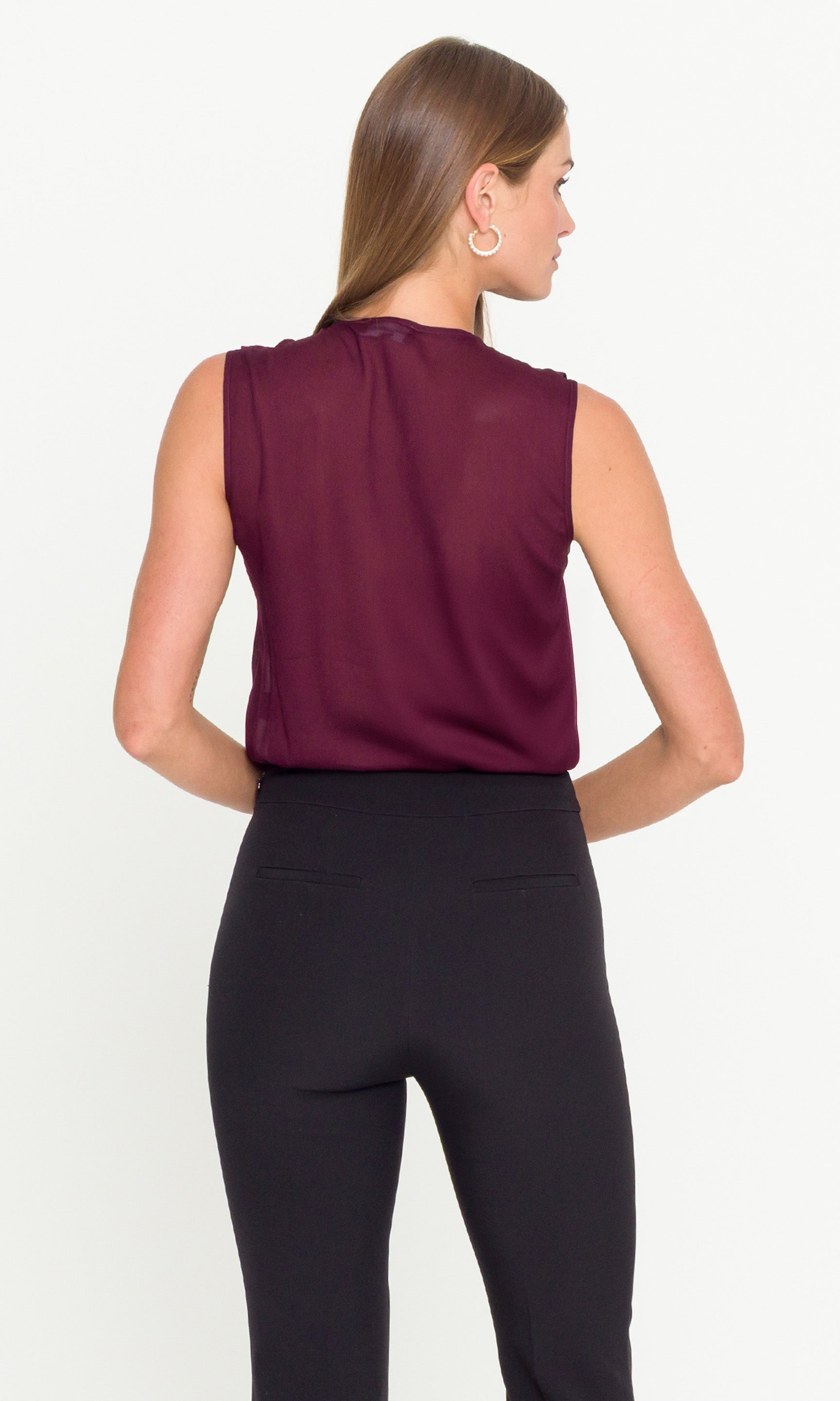 Back view of woman wearing a sleeveless burgundy top and black pants on a white background