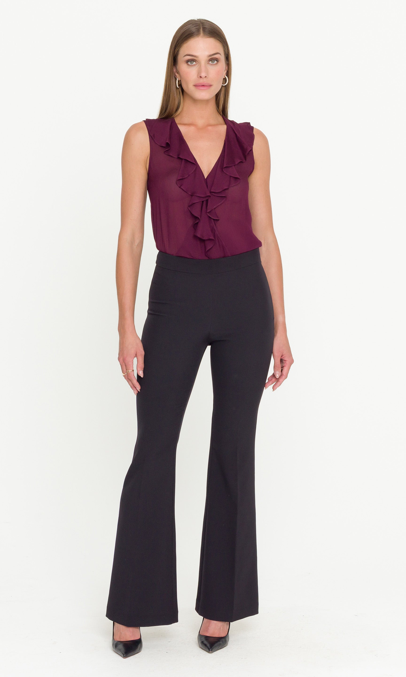 Full body image of model wearing a burgundy ruffled top and black pants on a white background