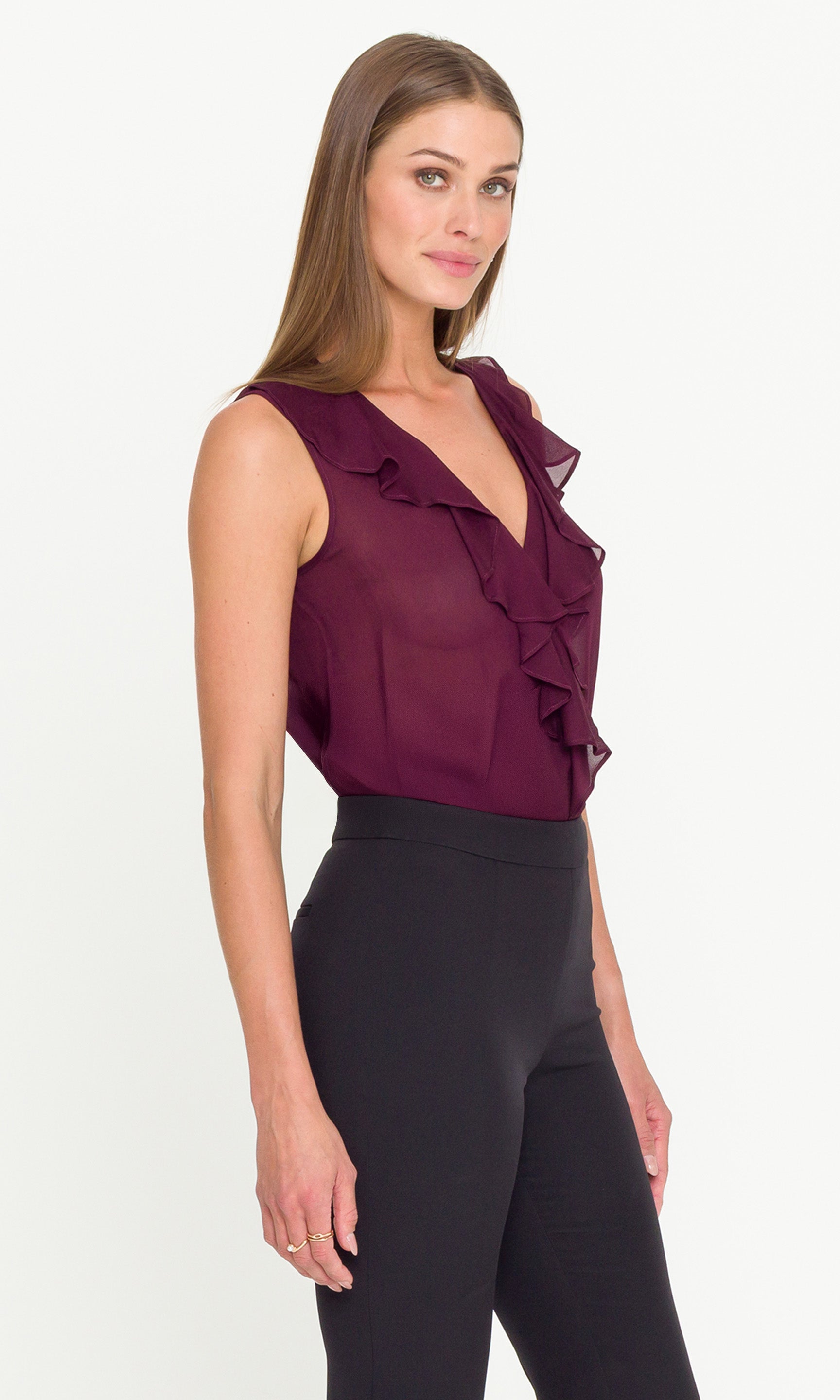 Side view of woman wearing a burgundy ruffled blouse and black pants on a white background
