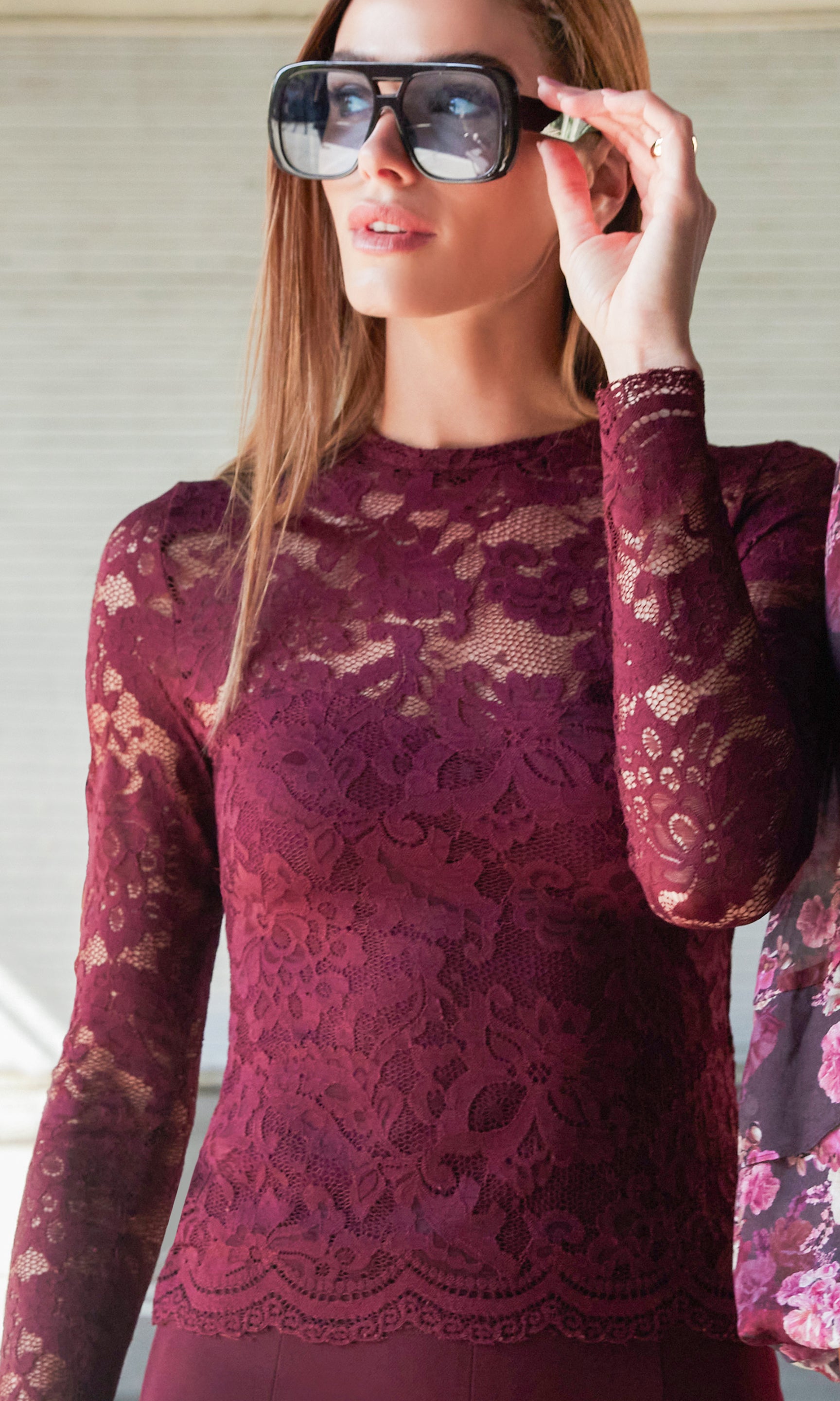 Woman wearing a burgundy lace top and sunglasses indoors.