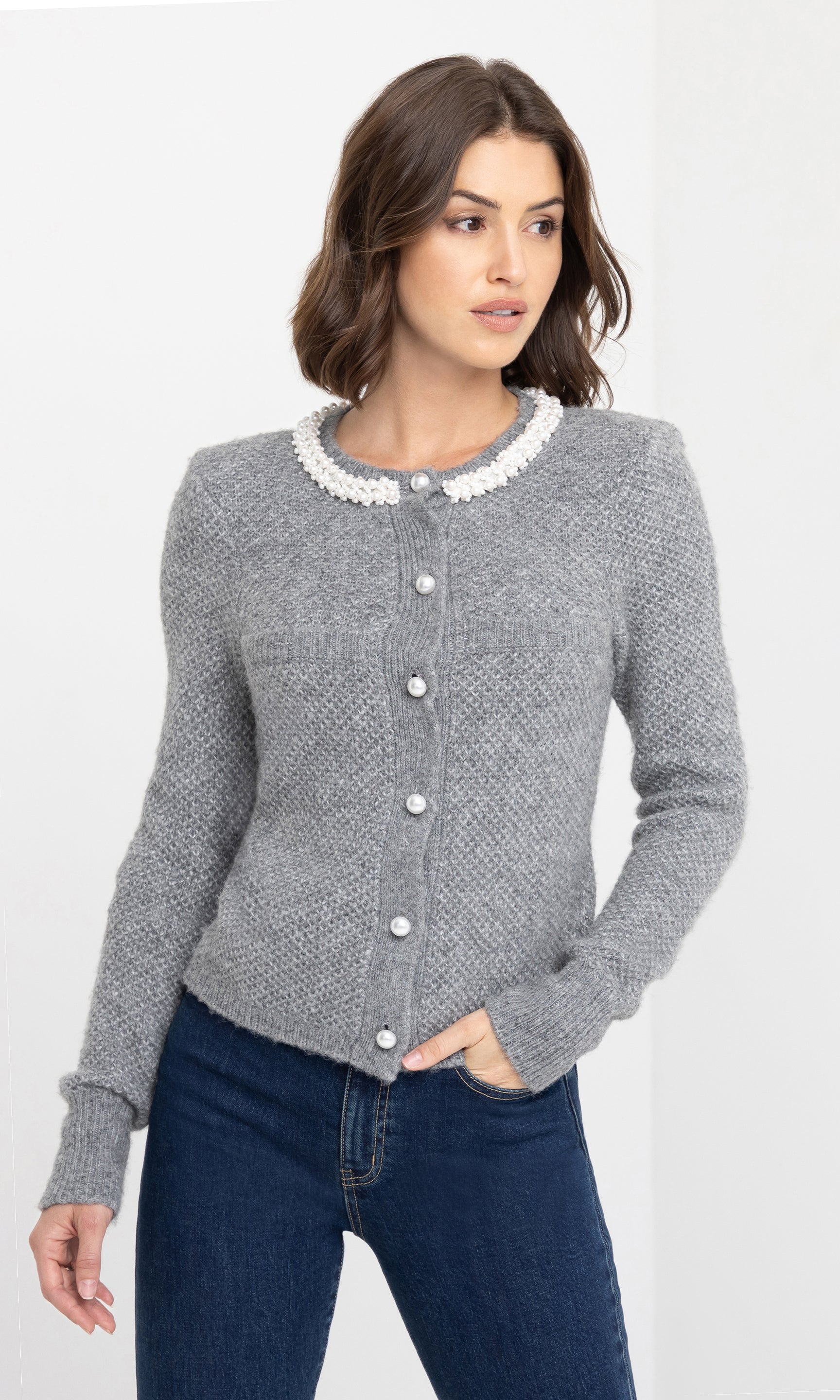 Front view of the model wearing the Clove Cardigan in grey, featuring a white pearl-trimmed collar and pearl button closures, styled with dark blue jeans.