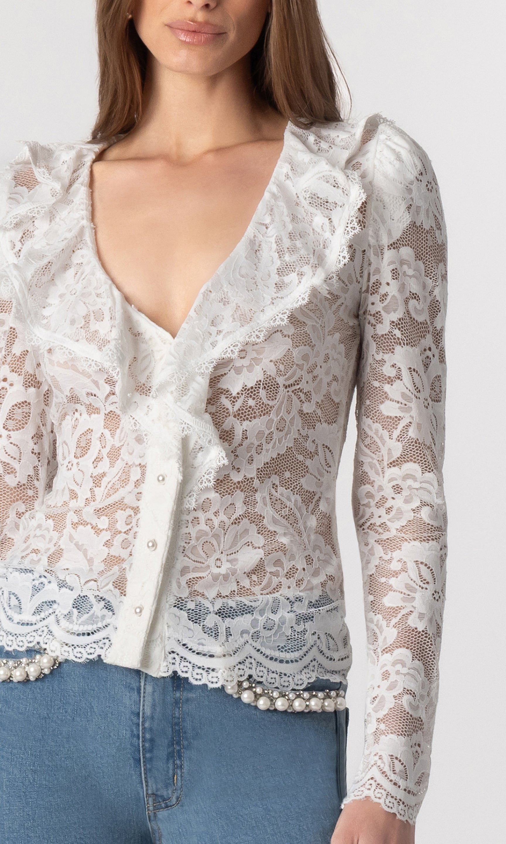zoomed in image of model wearing the Corsa lace top in white paired with blue jeans, showcasing the white lace detail all over with a ruffle neckline and small pearl buttons down the front