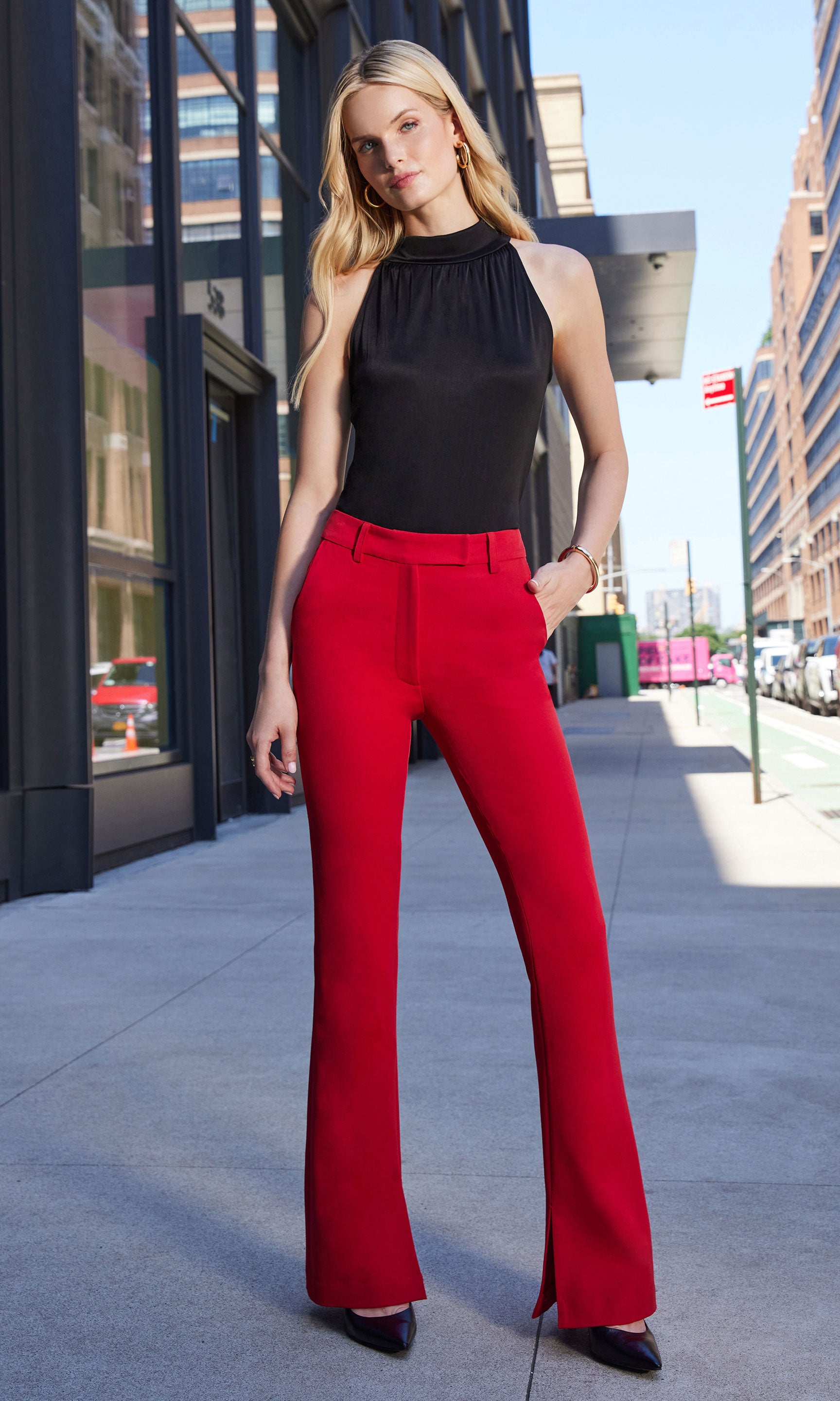 Woman wearing a black top and red pants standing on a city street.
