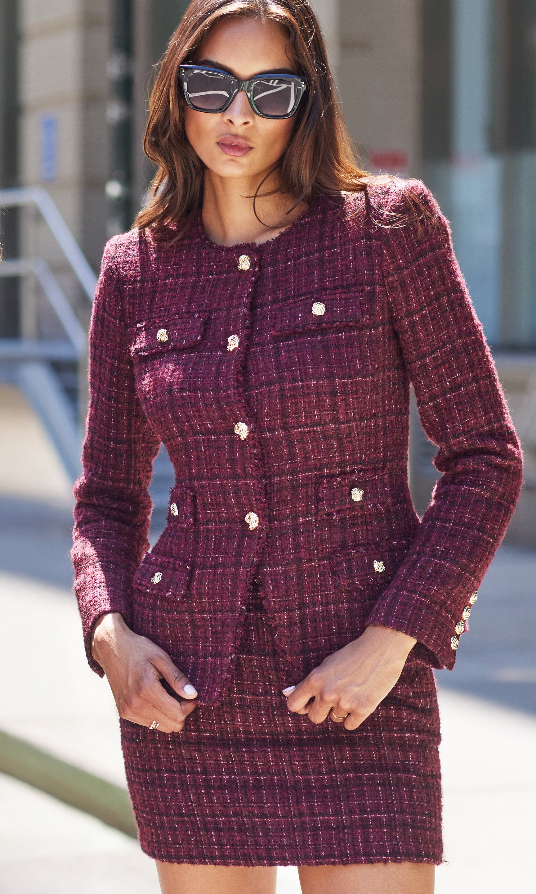 Woman wearing a burgundy tweed suit with sunglasses outdoors.