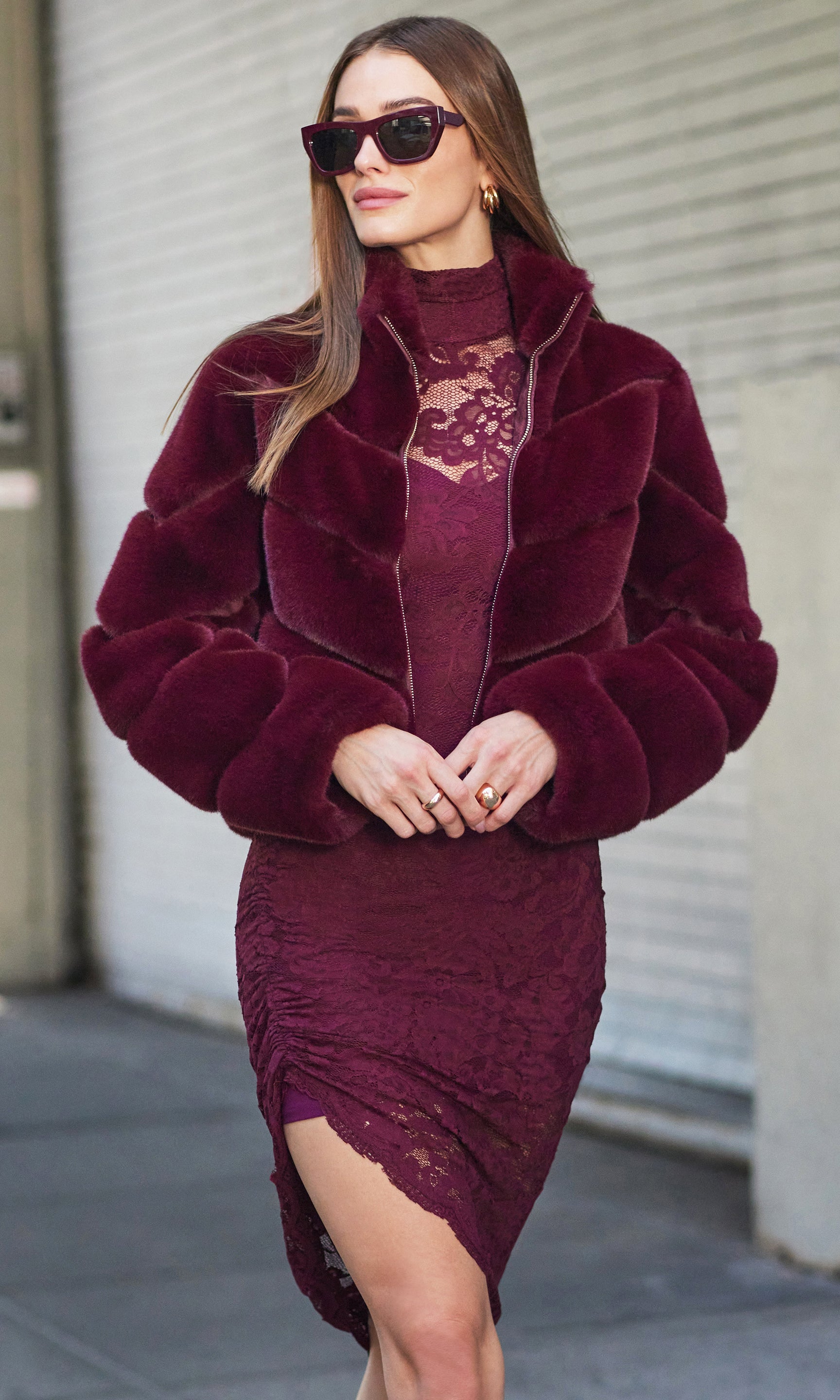 Woman wearing a burgundy fur coat over a matching dress with a lace detail.