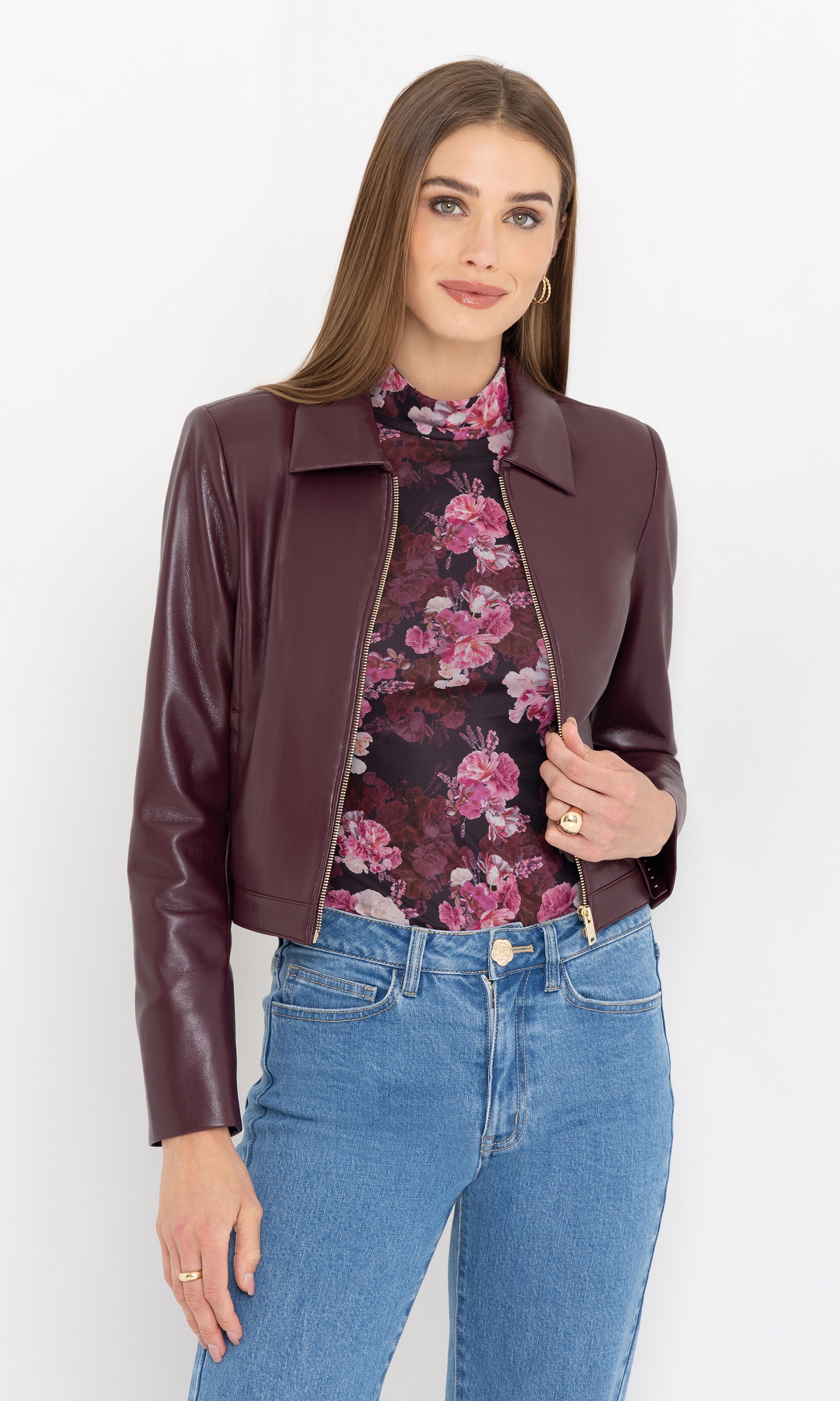 Woman wearing a cabernet vegan leather jacket, floral top, and blue jeans on a white background
