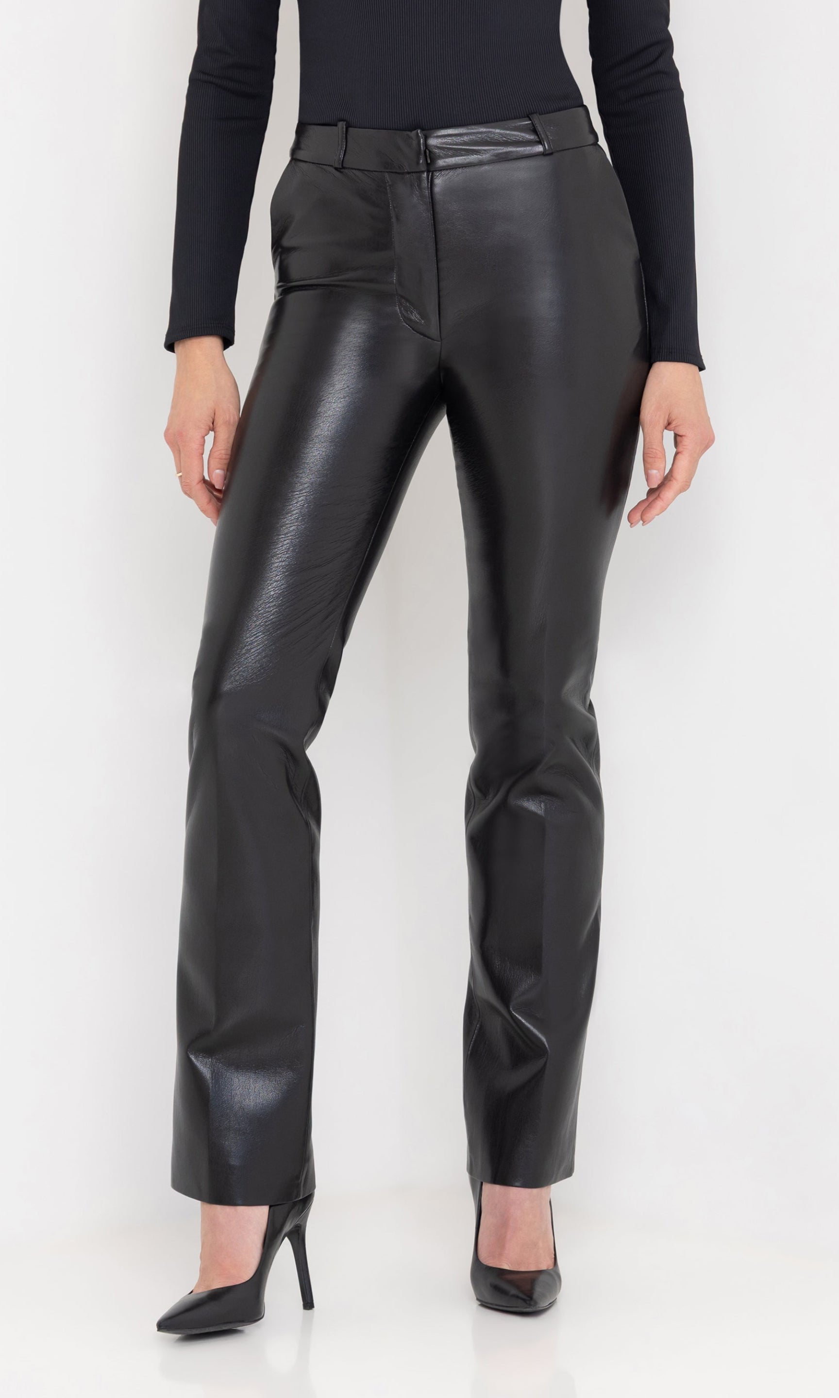 Close-up front view of the Lynette Vegan Leather Pants in black, styled with a black ribbed top and black pointed-toe heels.