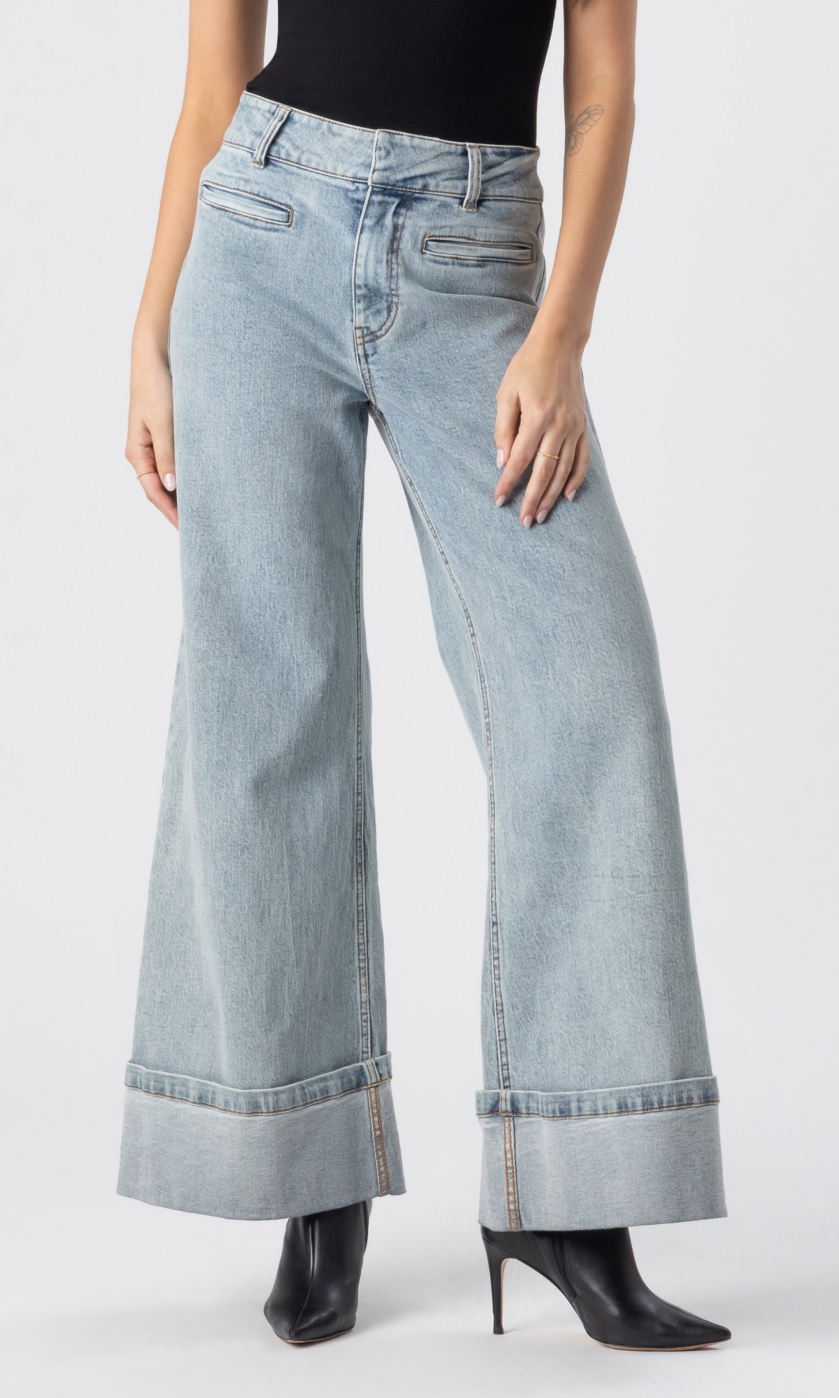 cropped image of model wearing the Raquel denim jeans in light blue, paired with a black tank and black heeled booties