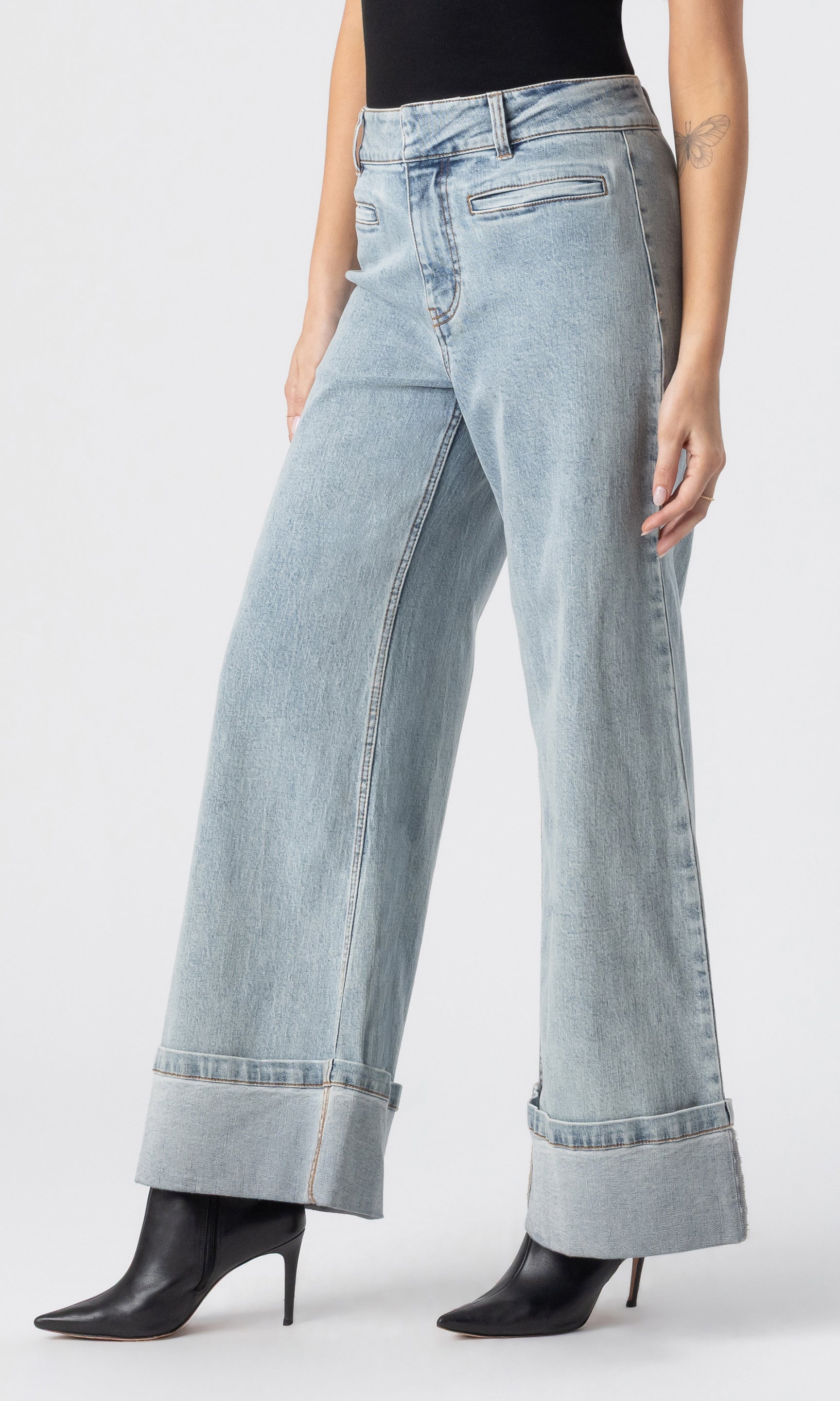 cropped side view image of model wearing the Raquel denim jeans in light blue, paired with a black tank and black heeled booties