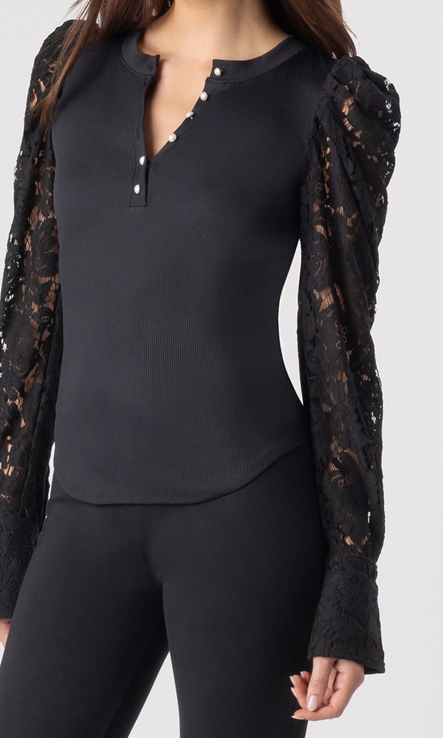zoomed in image of model wearing the Macoy top in black showcasing the small perls buttons on the chest and lace long sleeves, paired with matching black leggings