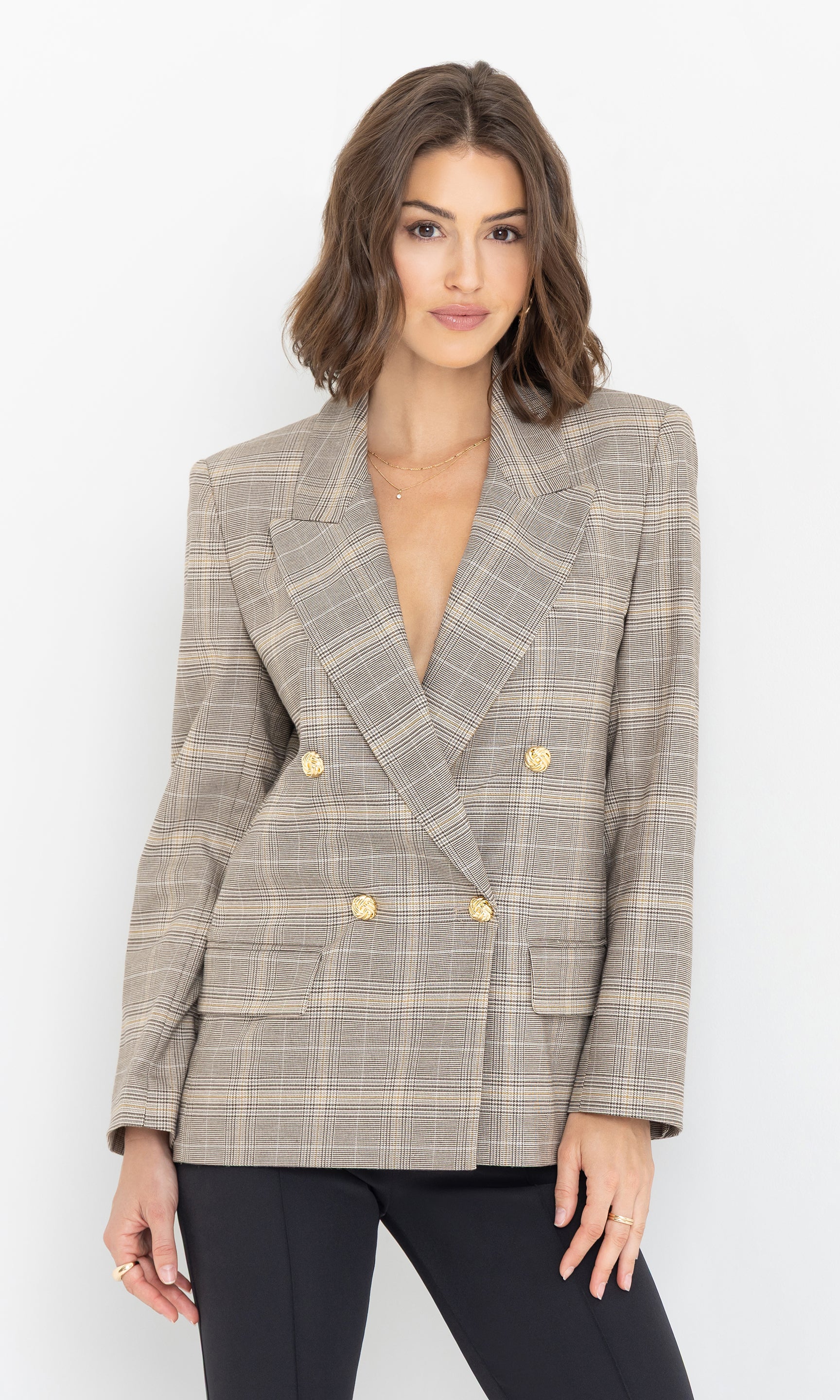 The model wears the Maverick Plaid Blazer in a beige and grey check pattern, styled with slim black pants, front view.