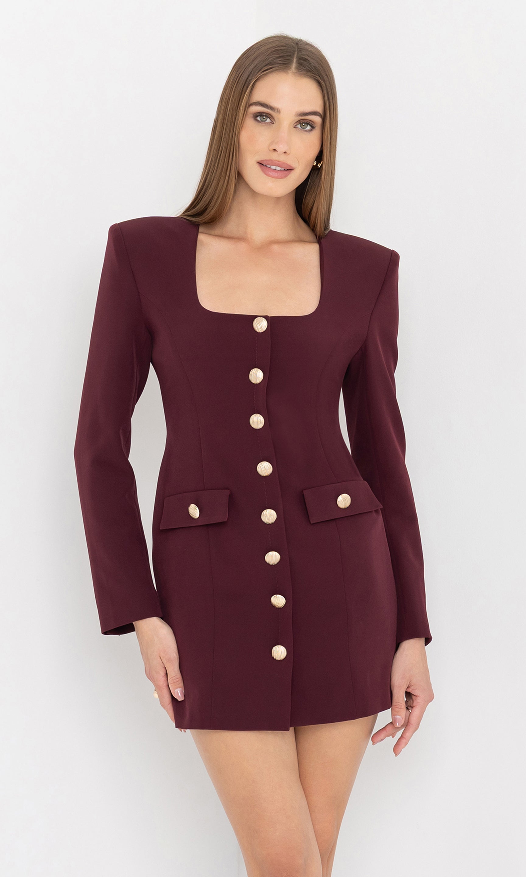 The model wears the Mellie Crepe Dress in a deep burgundy hue with a square neckline and gold button detailing, front view.