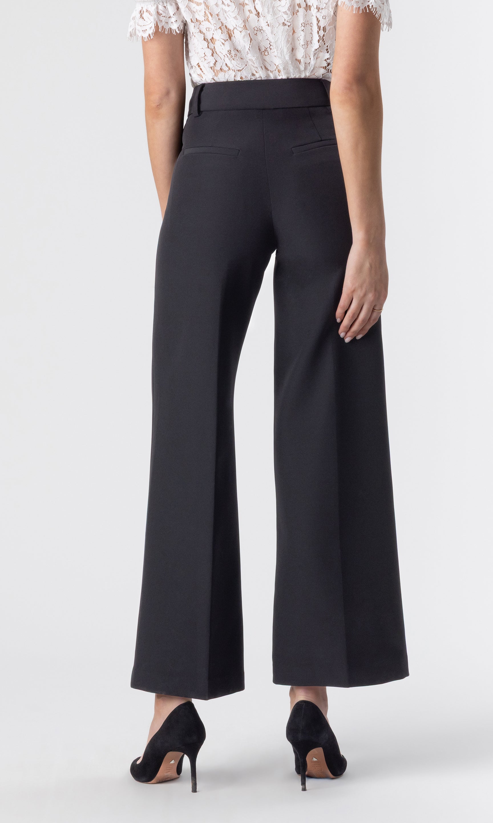cropped back view image of model wearing a white lace top paired with the Rayne crepe wide-leg pants with black heels