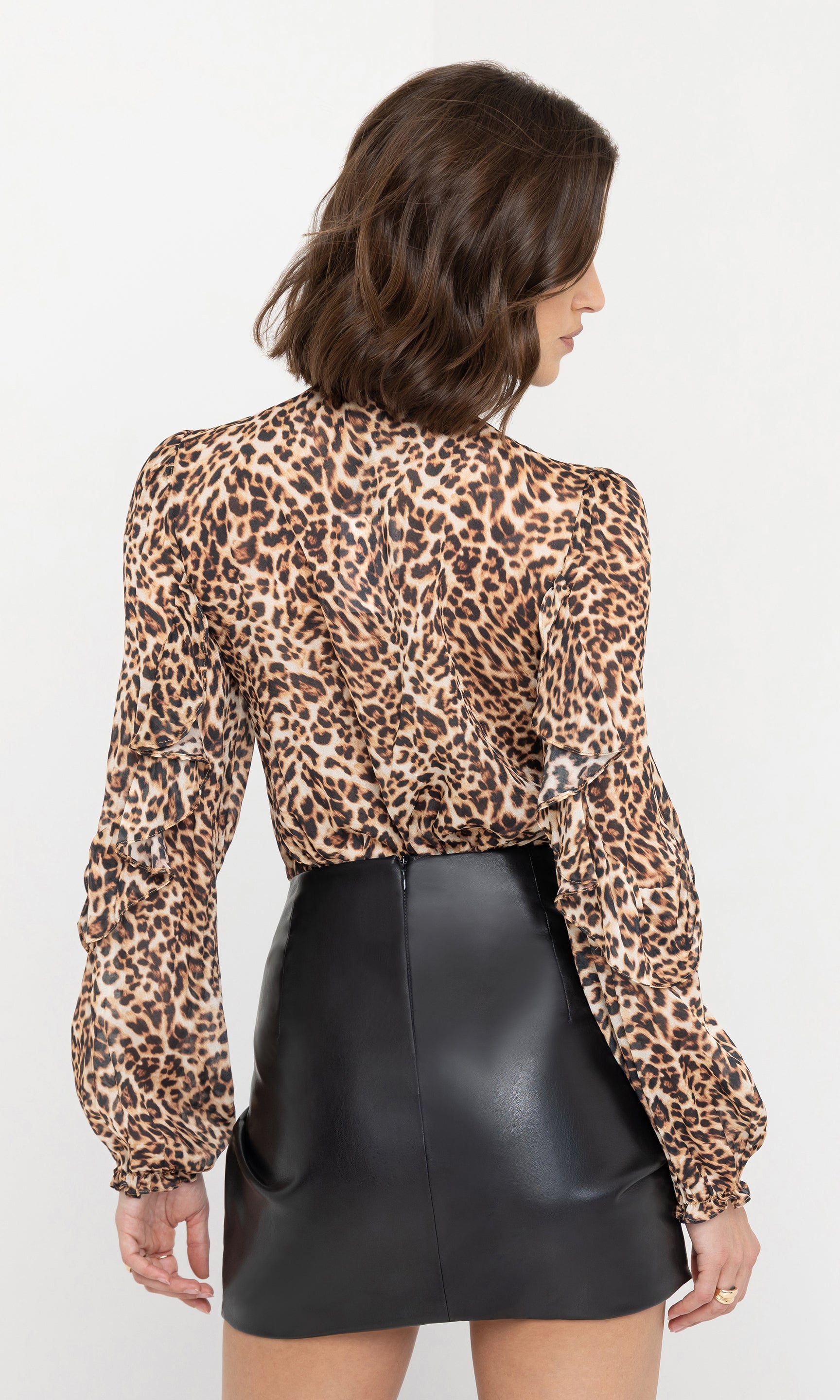 Rear view of the model showcasing the back design of the Nikali Leopard Wrap Bodysuit paired with a black leather mini skirt.