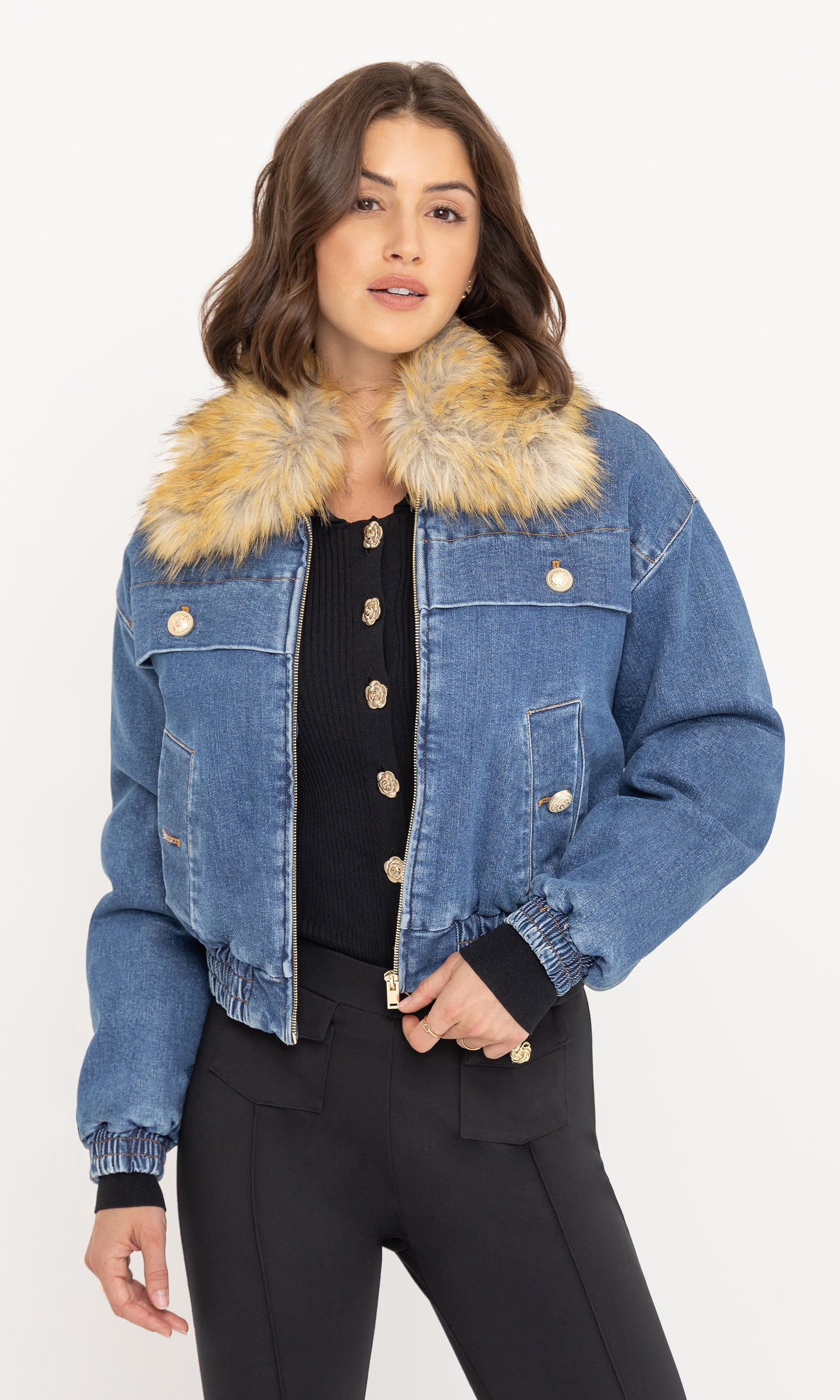 Front view of the model wearing the Paco Denim Bomber with a light brown faux fur collar, paired with a black buttoned top and black trousers.