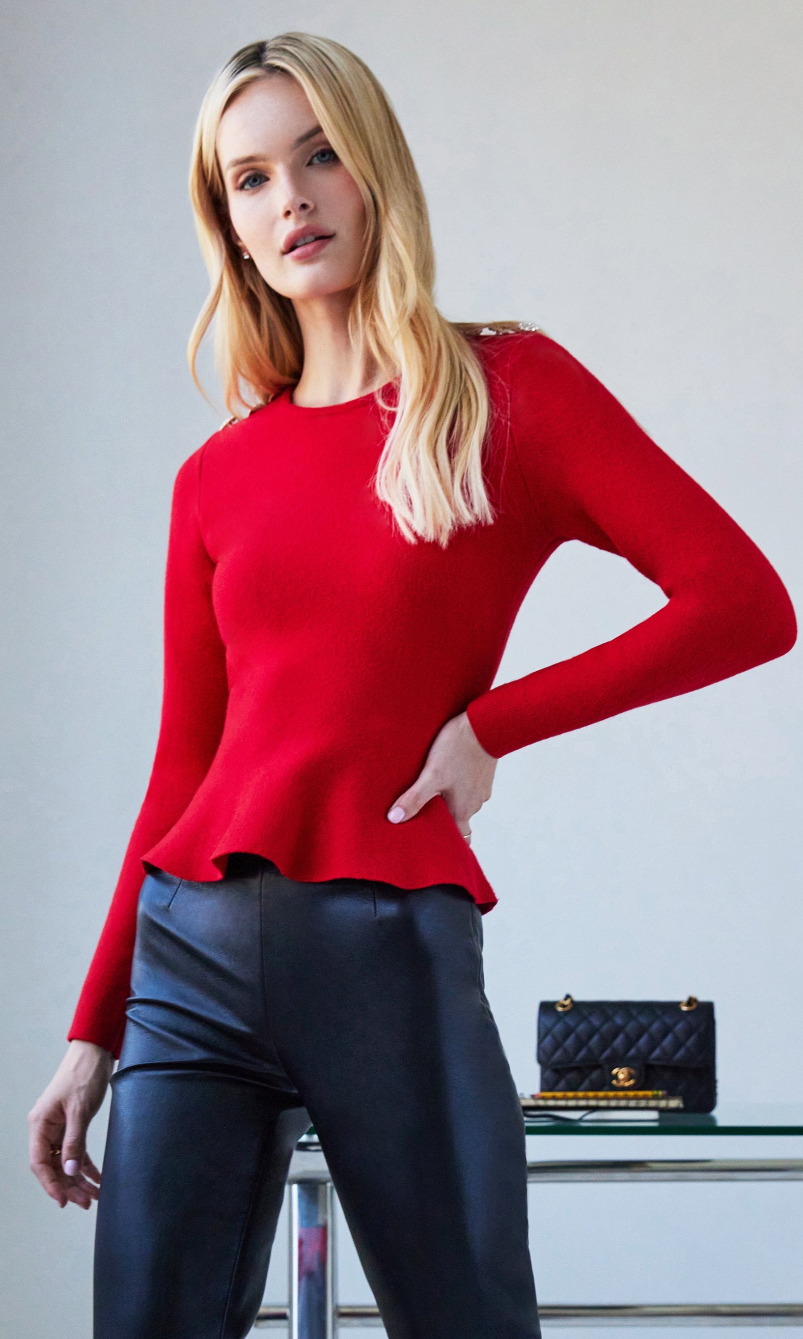Woman wearing a red sweater and black pants with a handbag on a gray background