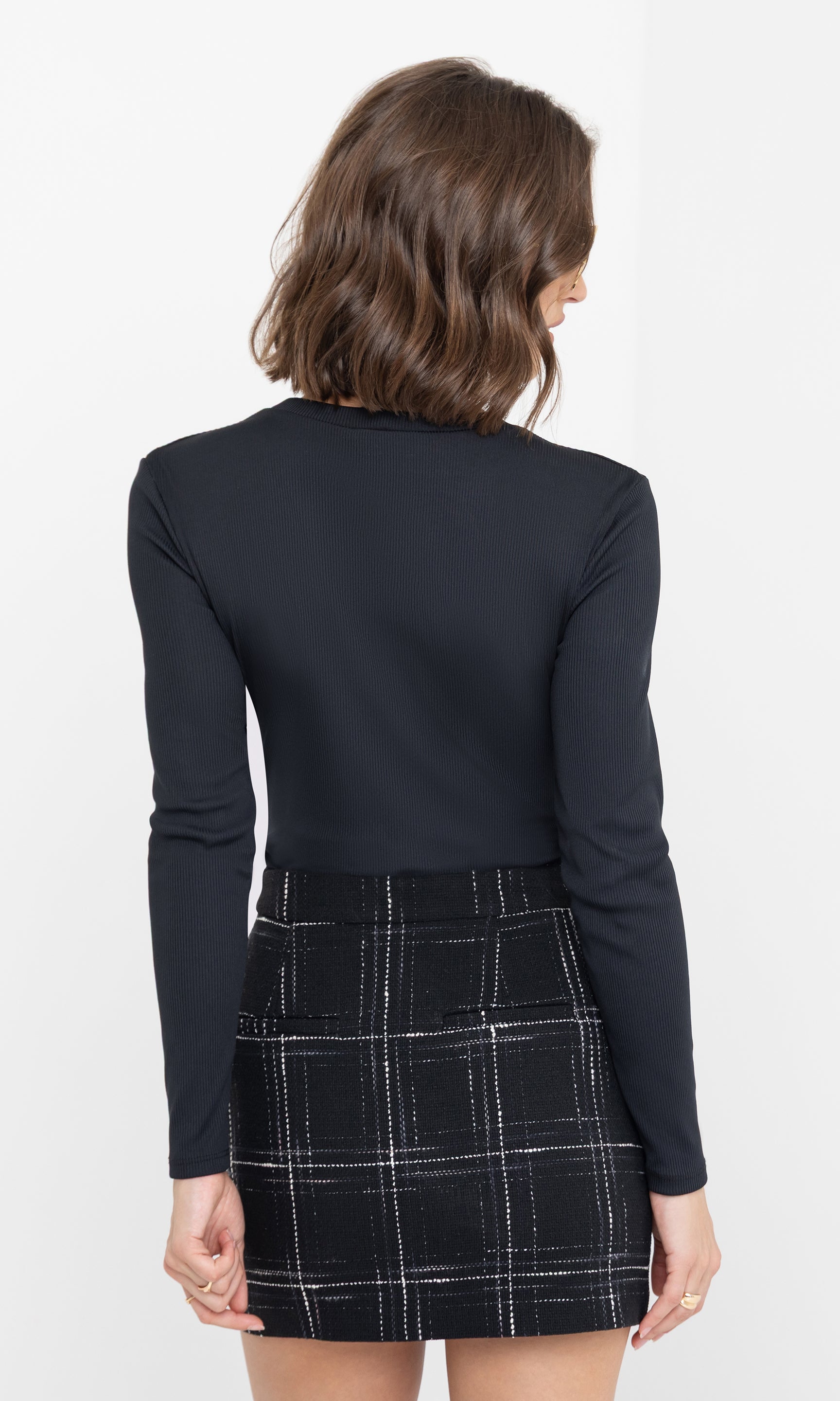 Rear view of the model wearing the Patton Rib Top with long sleeves and a fitted silhouette, paired with a black plaid mini skirt.