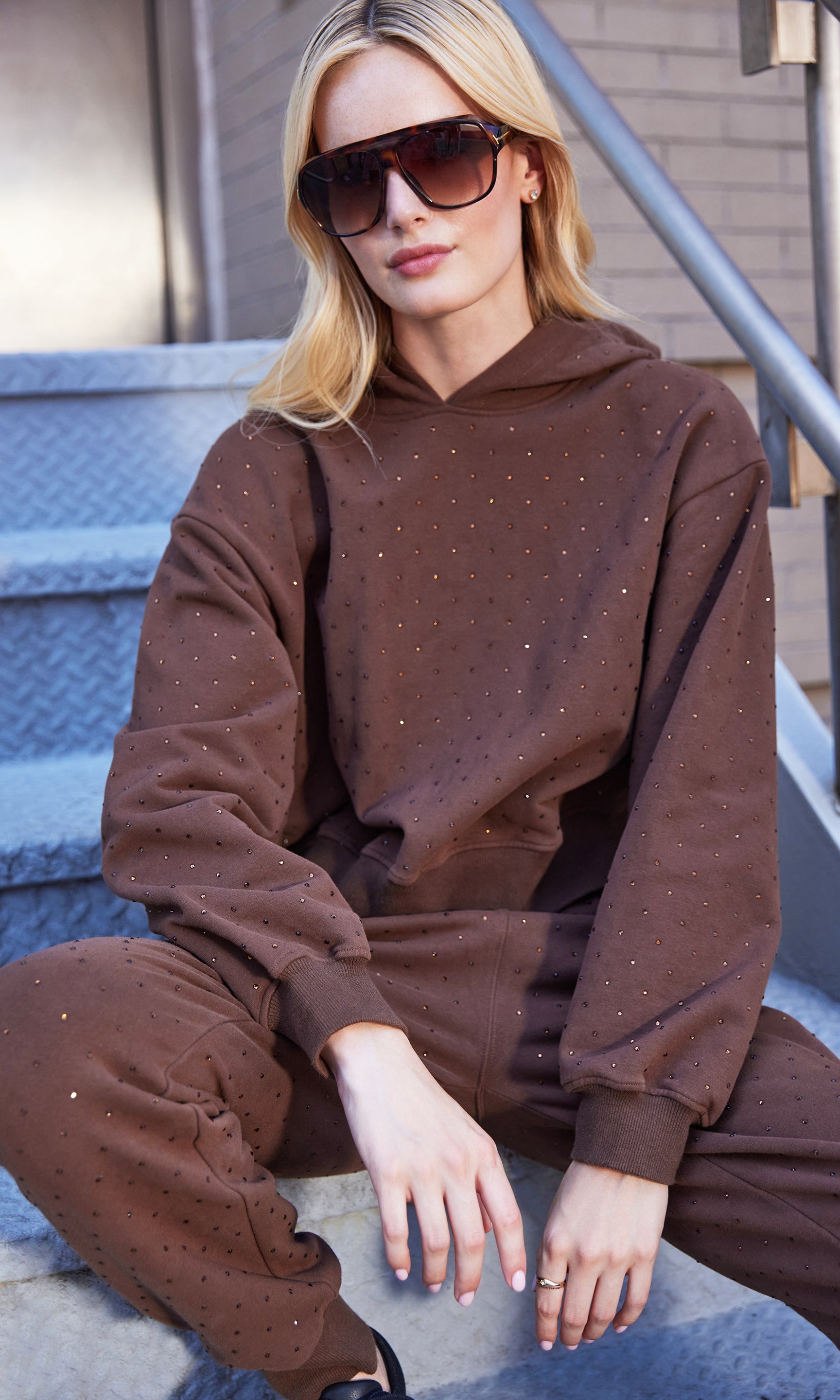 Person wearing a brown hoodie and pants sitting on steps.