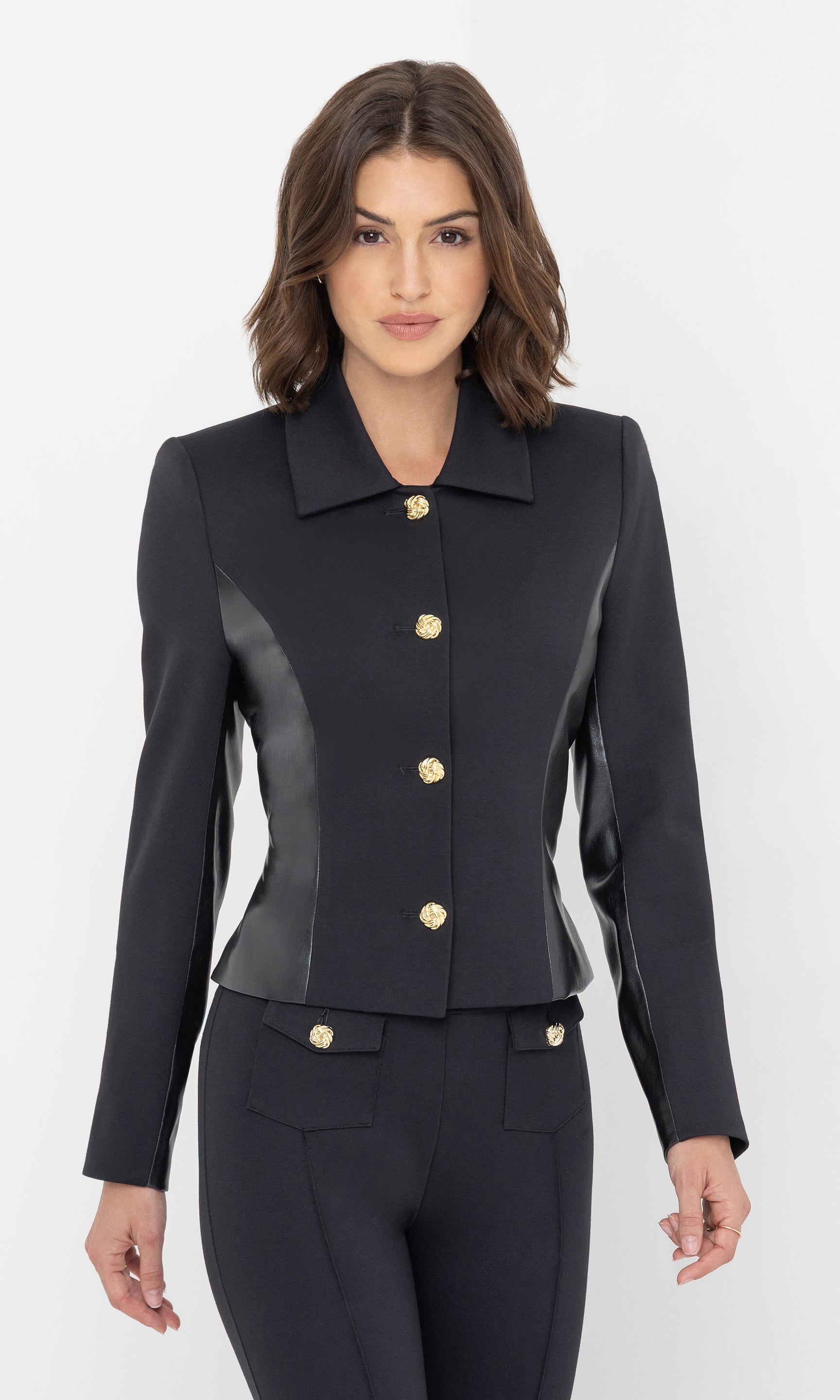 The model poses in the Robby Vegan Leather Combo Ponte Jacket in black from a three-quarter front view, focusing on the structured shoulders and sleek finish.