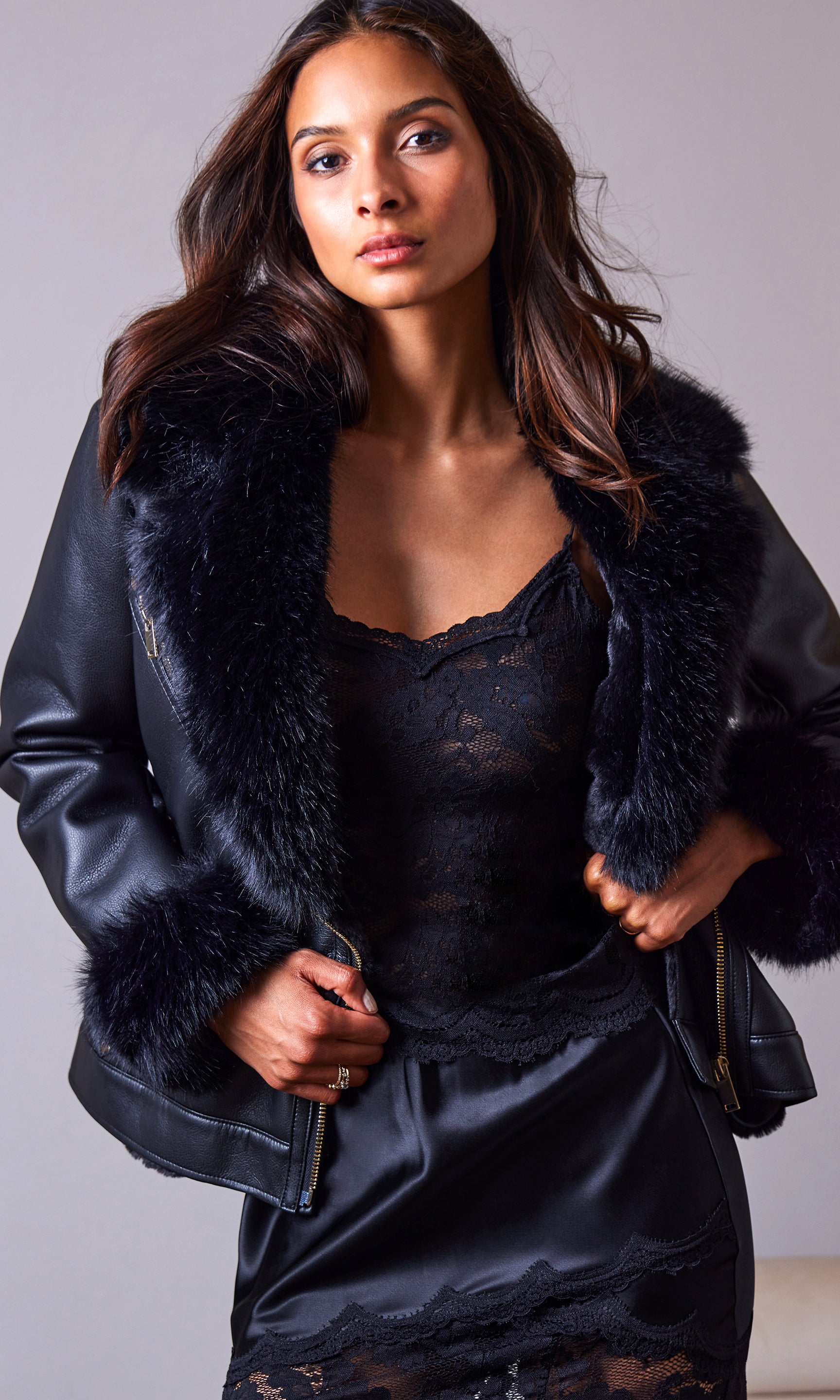 Woman wearing a black leather jacket with fur trim against a gray background