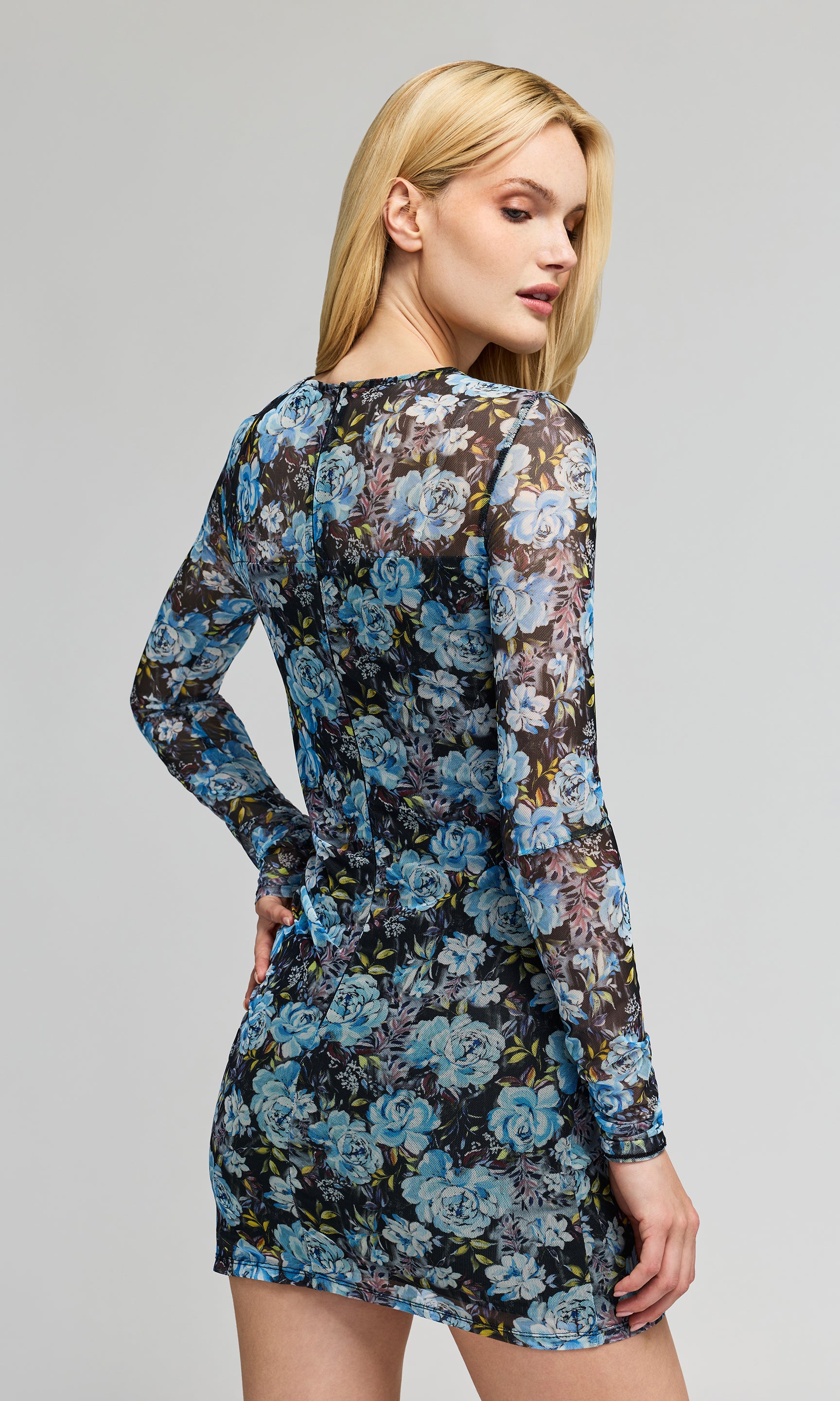 Back view of woman wearing a floral dress with long sleeves on a gray background