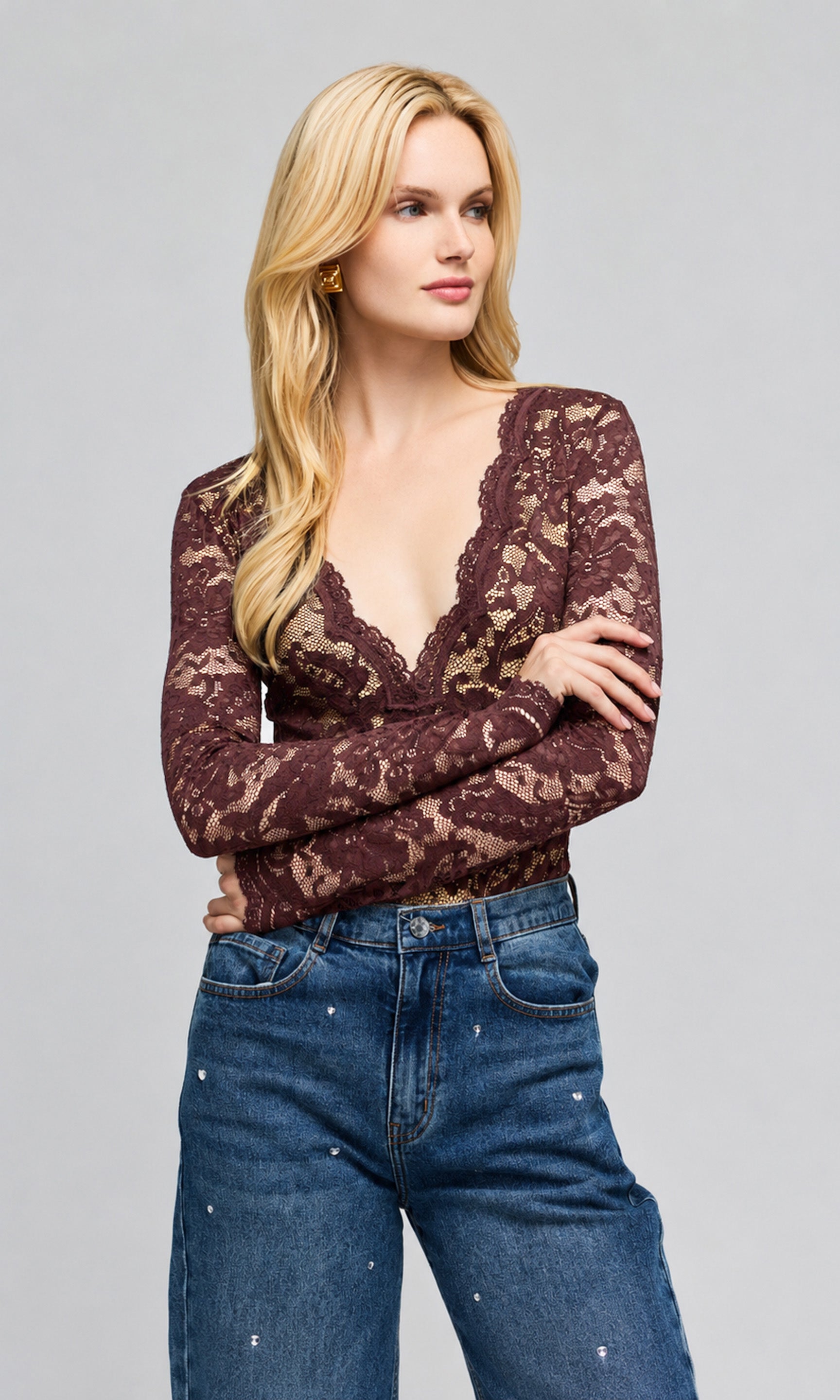 Model wearing a dark brown lace long-sleeve top with a deep V-neck and blue jeans, on a plain background.