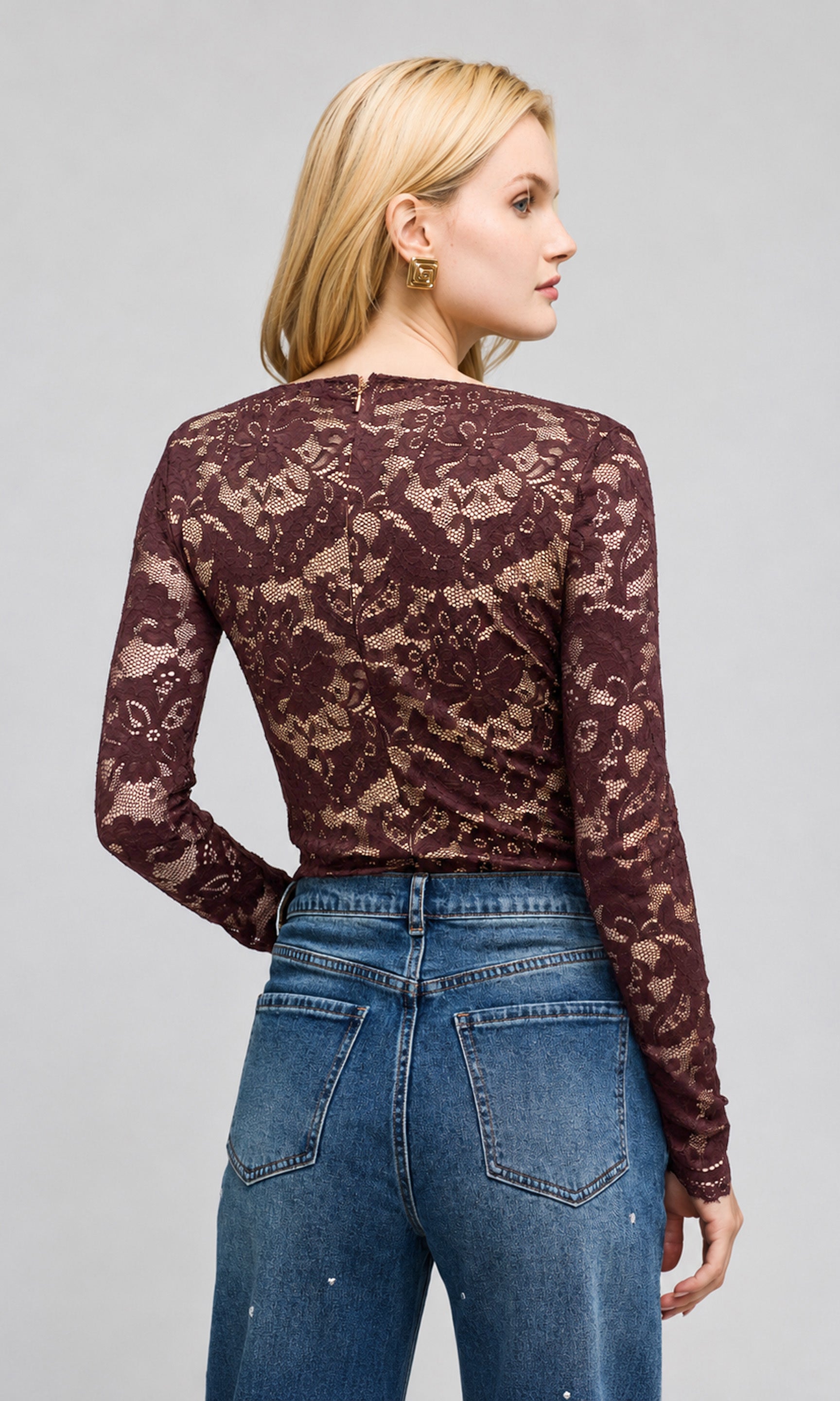 Back view of model wearing a dark brown lace long-sleeve top with a deep V-neck and blue jeans, on a plain background.