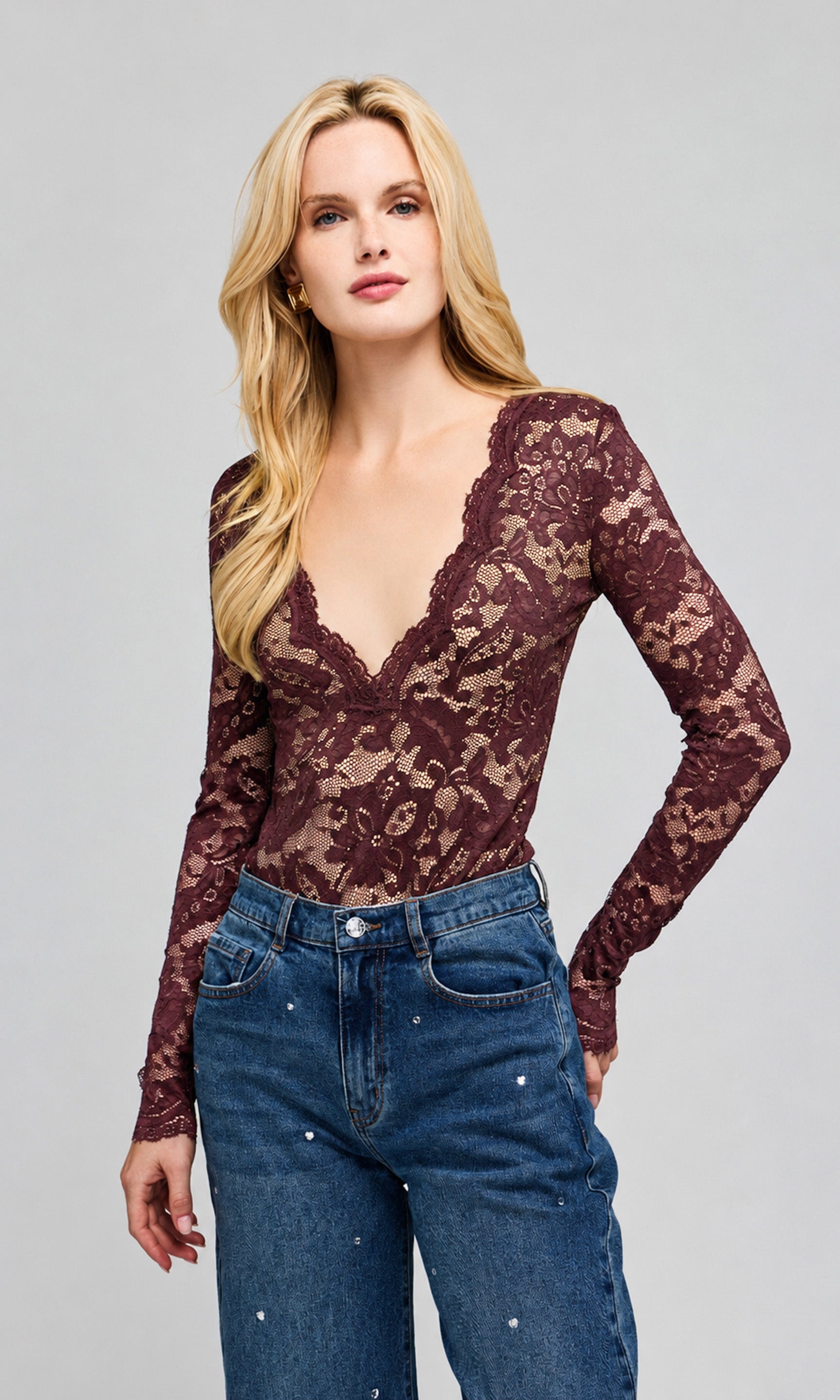 Side view of model wearing a dark brown lace long-sleeve top with a deep V-neck and blue jeans, on a plain background.