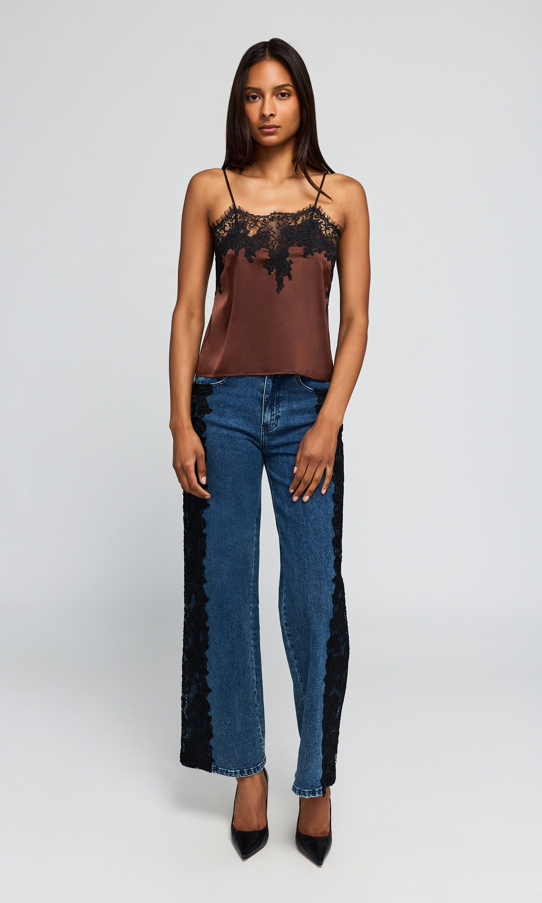 Model wearing a brown camisole top with black lace trim, blue jeans with black lace side panels, and black pointed heels.