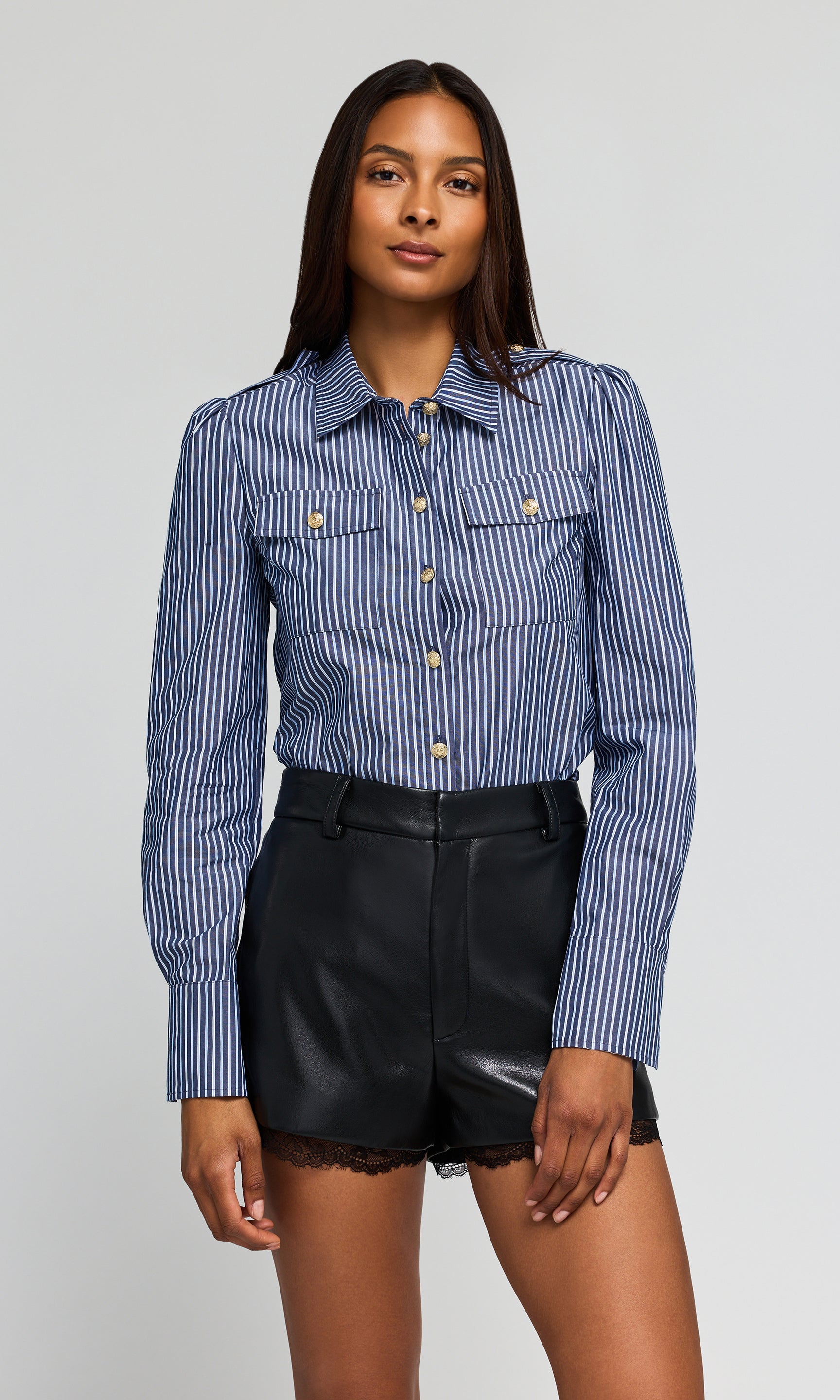 Model wearing a blue and white striped button-up shirt tucked into black shorts, on a plain background.