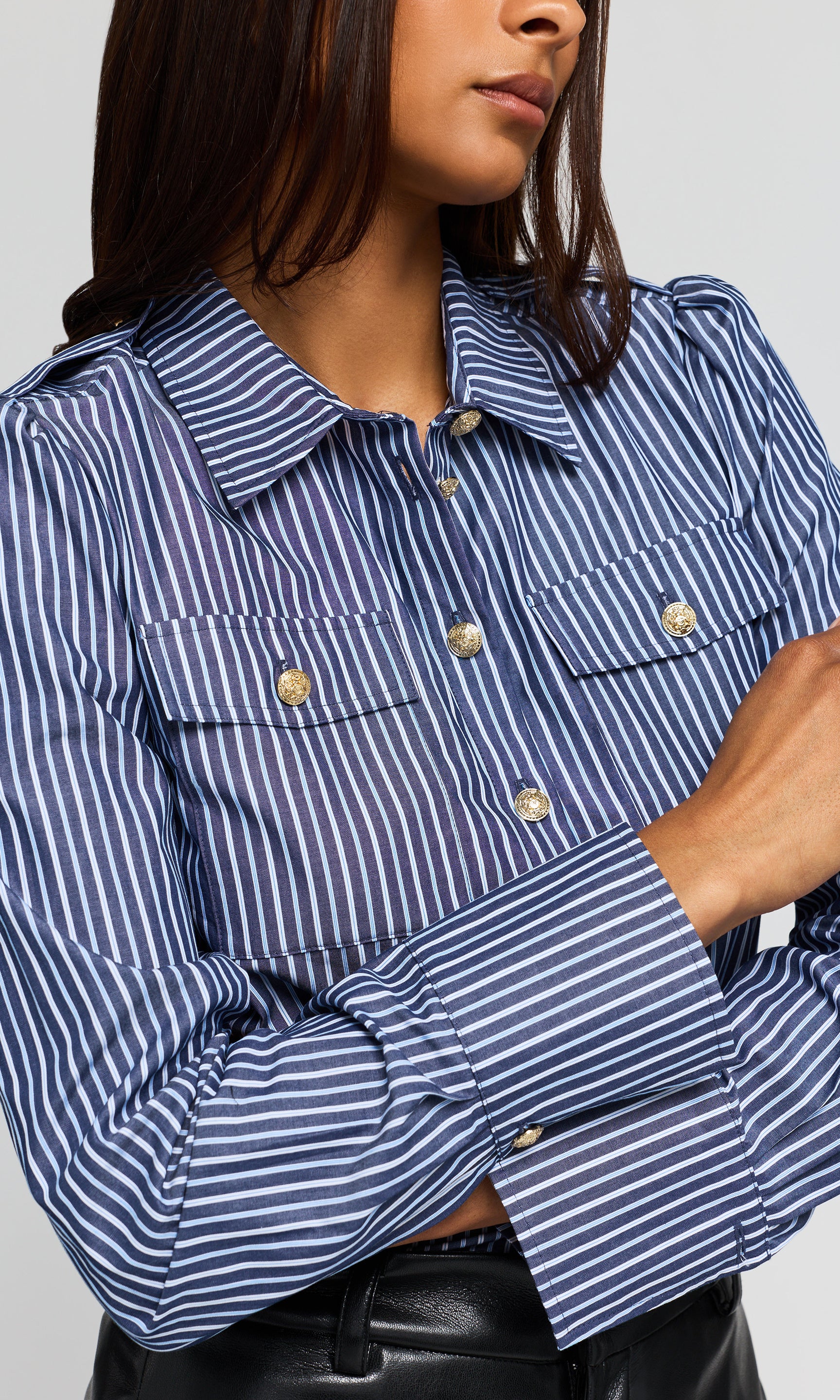 Close-up a blue and white striped button-up shirt with gold-tone buttons and chest flap pockets.