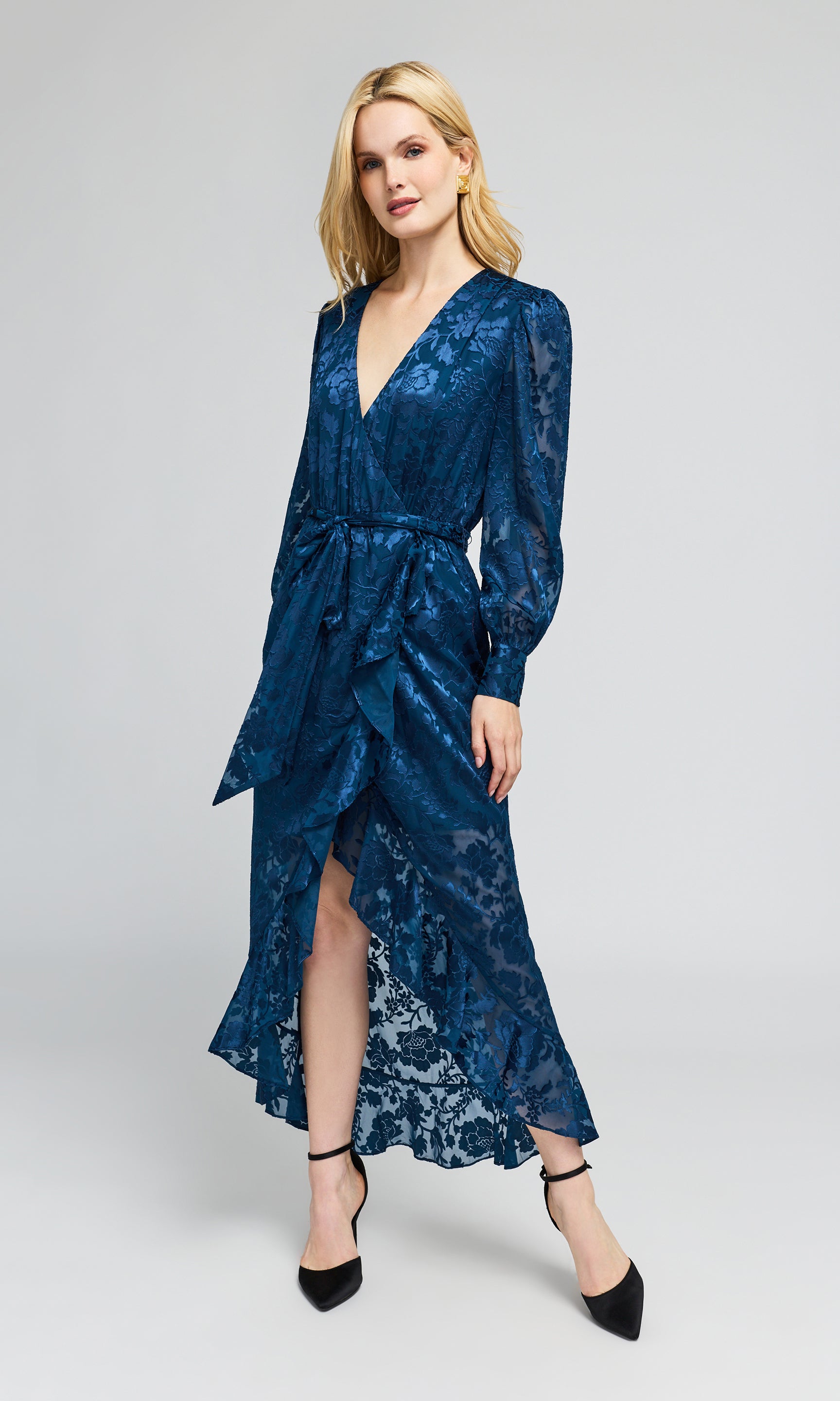 Side view of model wearing a long-sleeved wrap midi dress in a deep blue jacquard pattern with a matching tie belt.