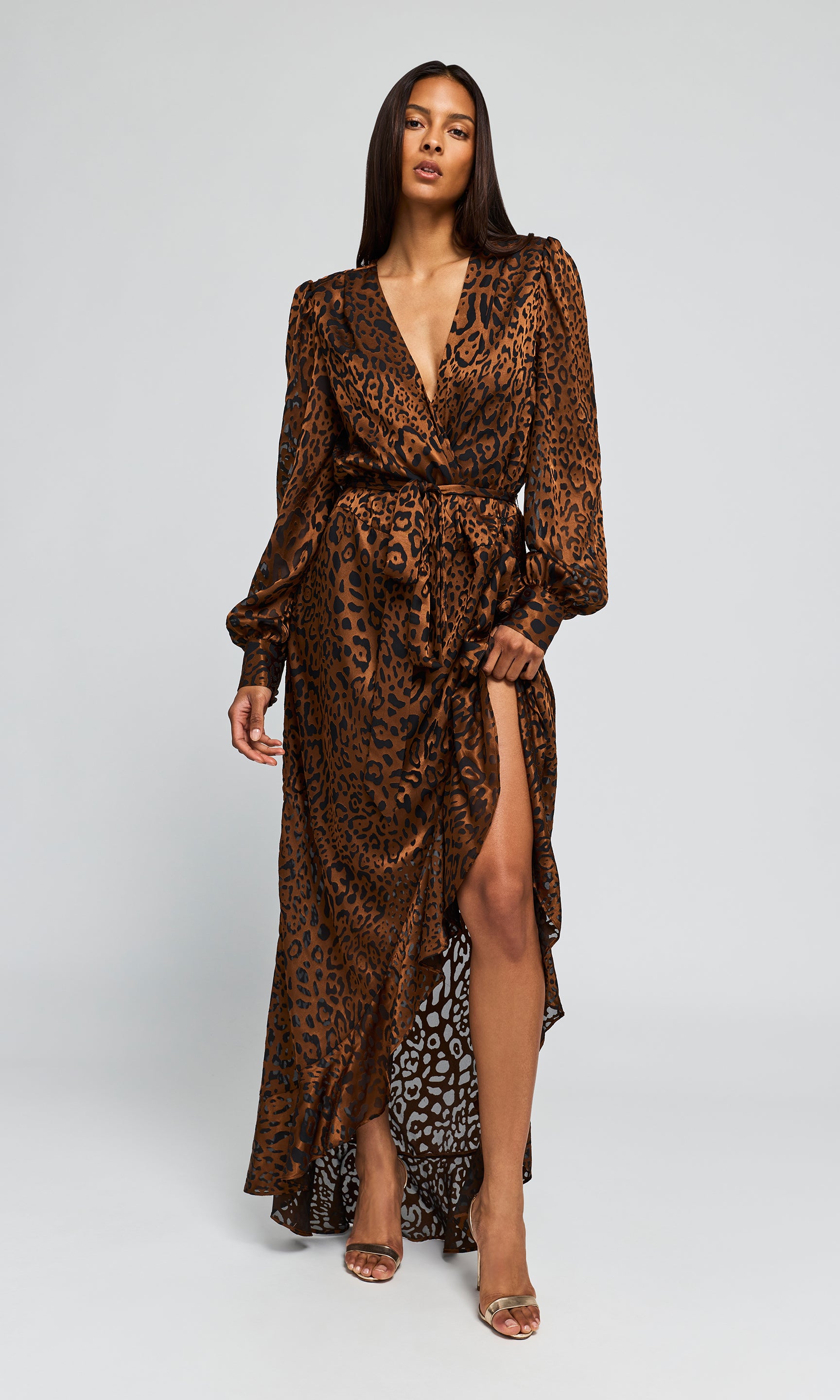 Model wearing a long brown leopard-print maxi dress with a high slit, paired with clear high-heeled.