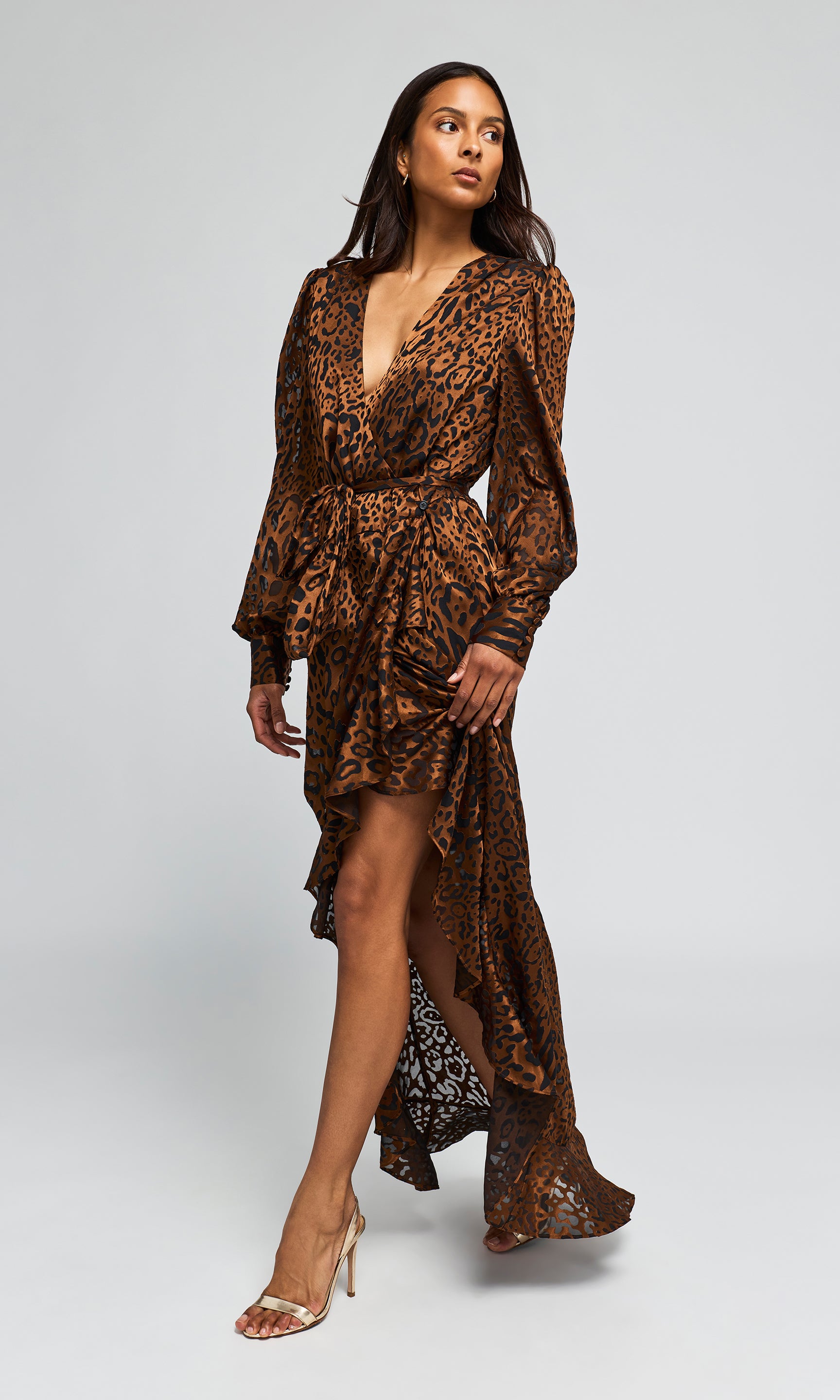 Side view of model wearing a long brown leopard-print maxi dress with a high slit, paired with clear high-heeled.