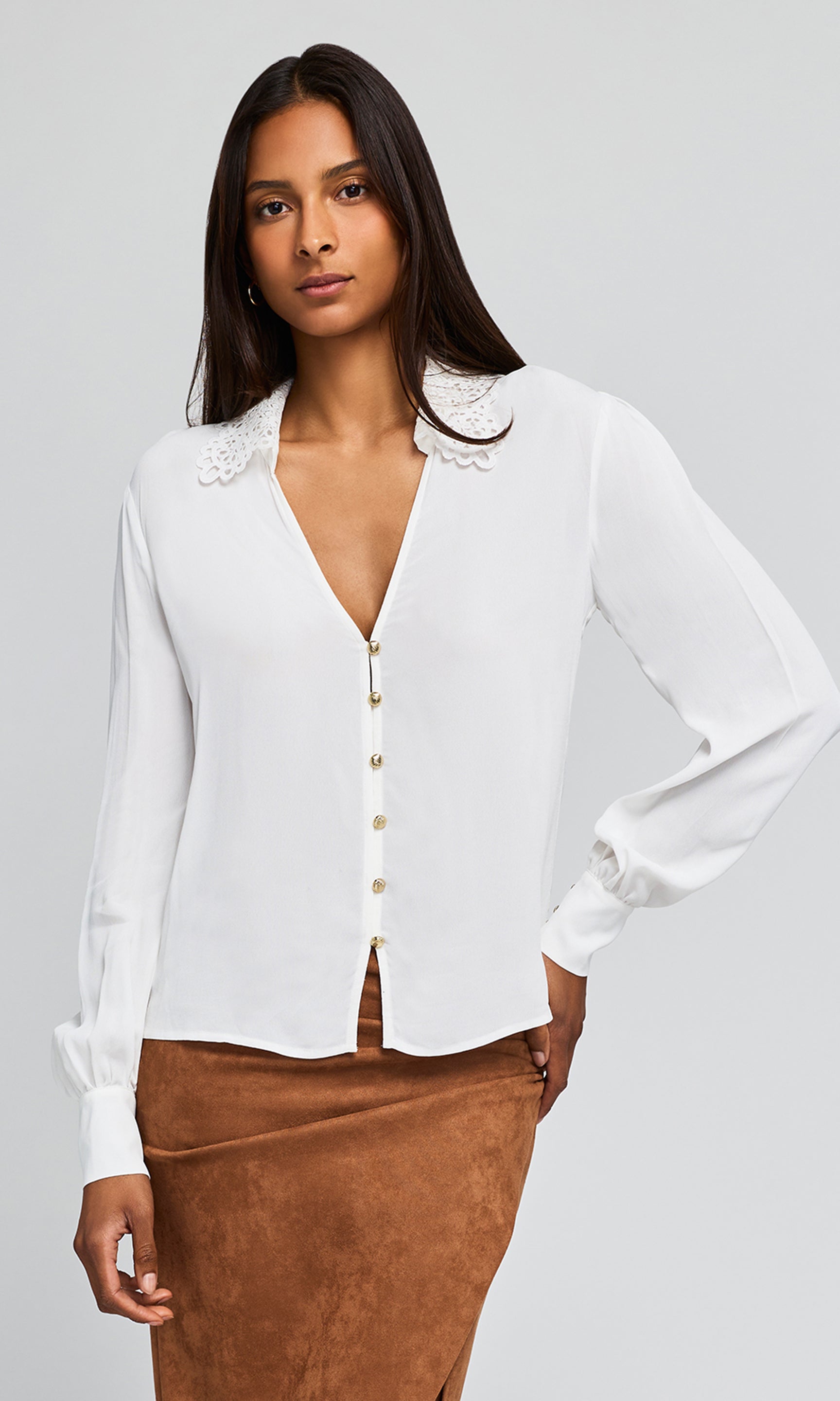 Model wearing a white blouse with  decorative lace detail at the collar, paired with a ruched brown skirt.