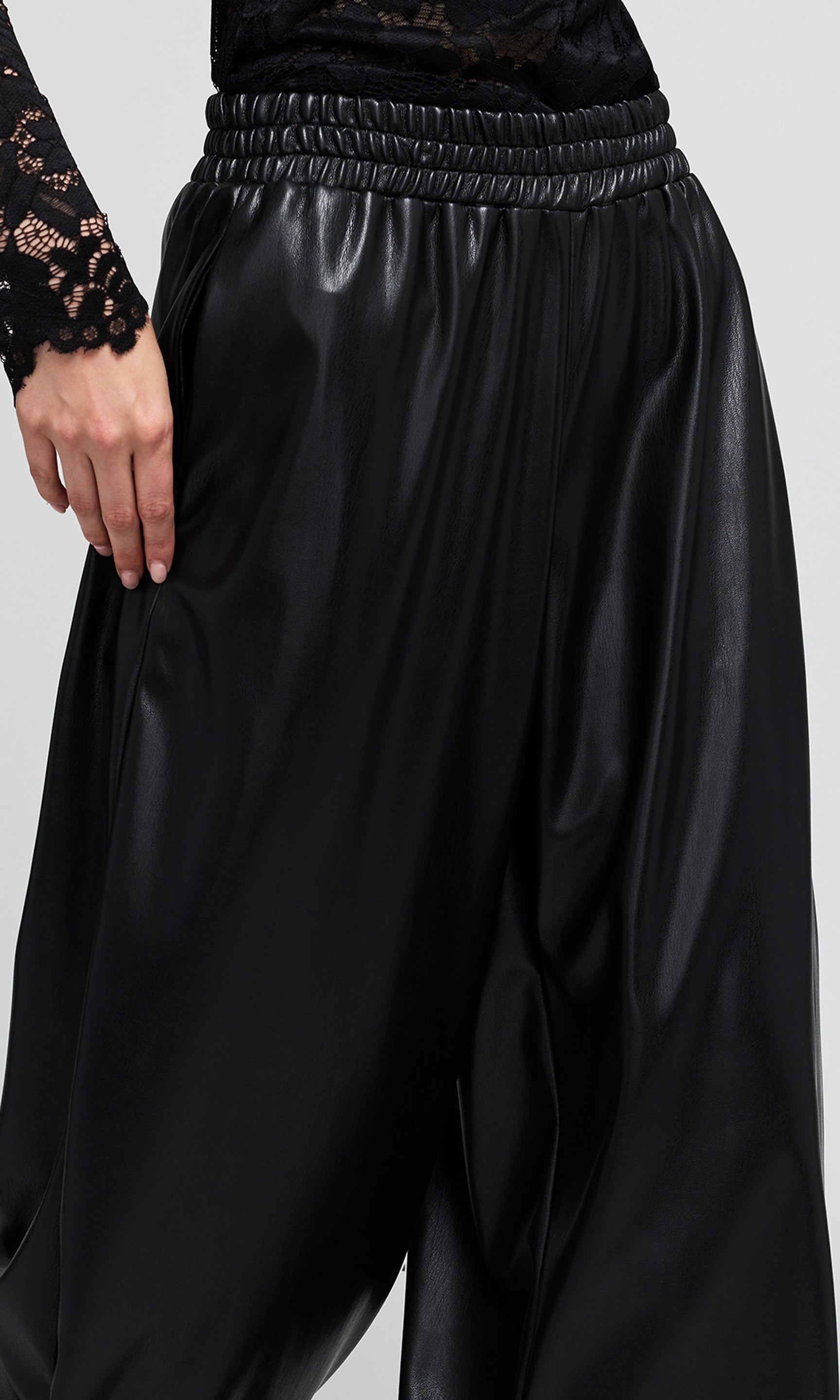 Close up of black vegan-leather black pants with an elastic waistband on a plain background.