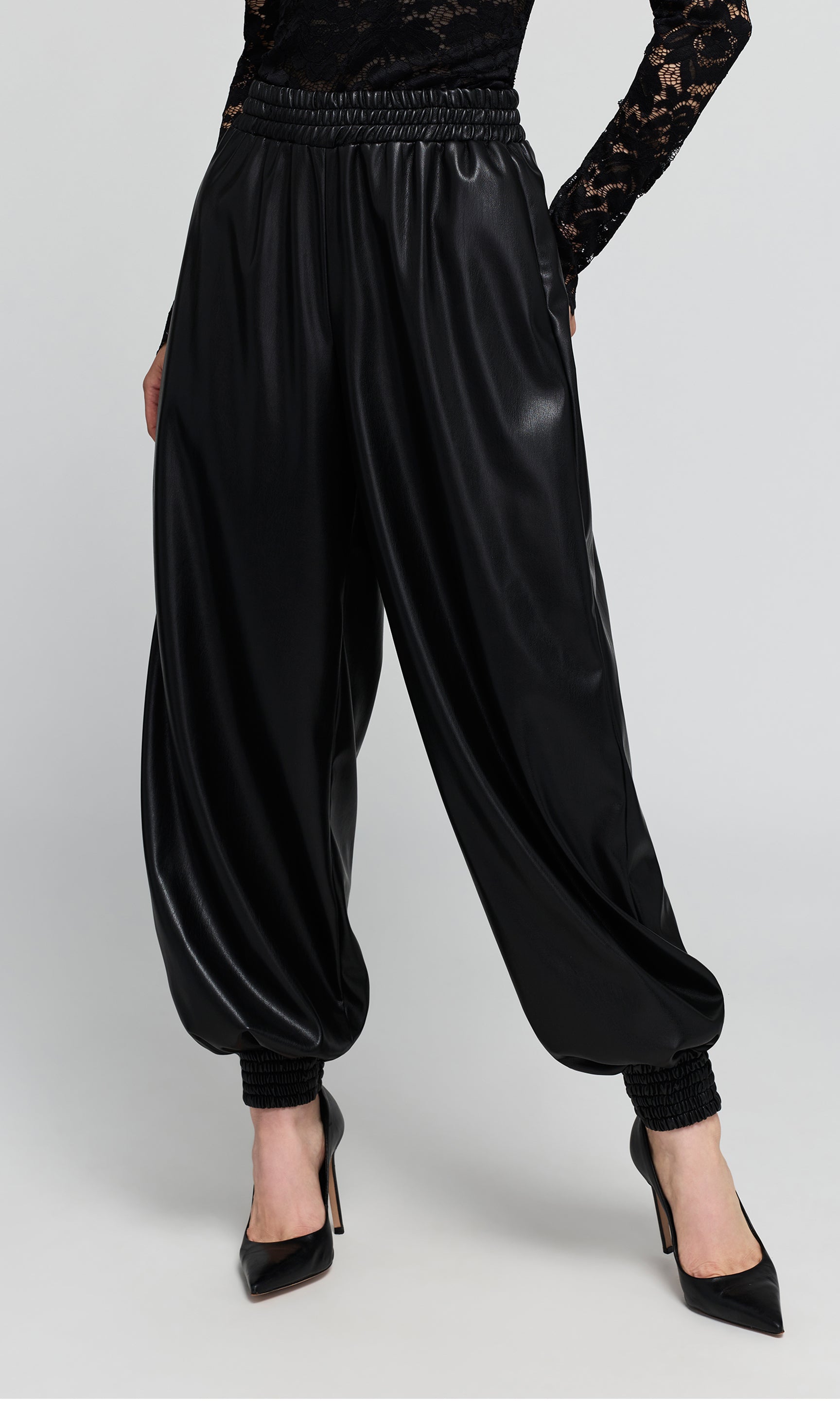 Side view of black vegan-leather, wide-leg harem pants with an elastic waistband, and gathered cuffs, shown on a model.