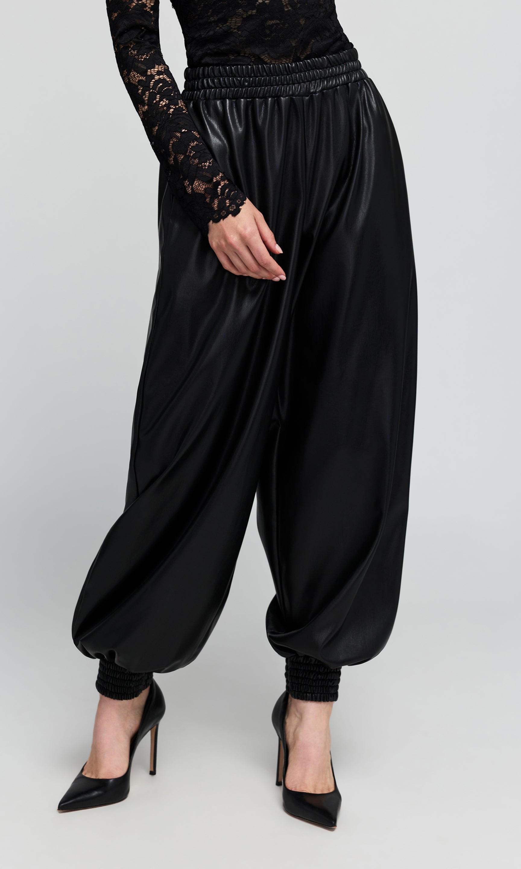 Side view of black vegan-leather, wide-leg harem pants with an elastic waistband, and gathered cuffs, shown on a model.