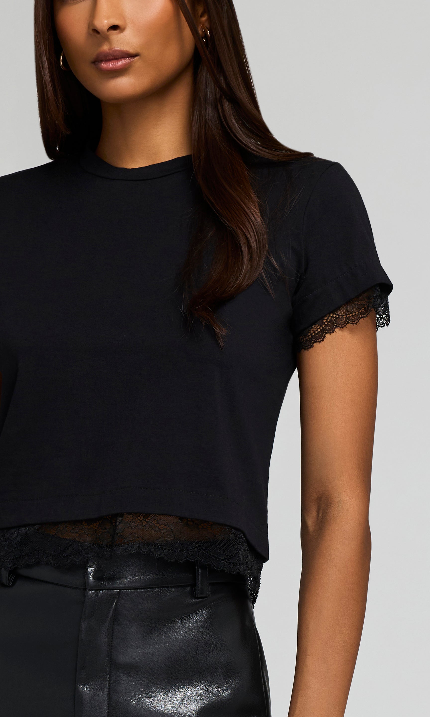 Black top with lace details on sleeves worn by a model against a neutral background