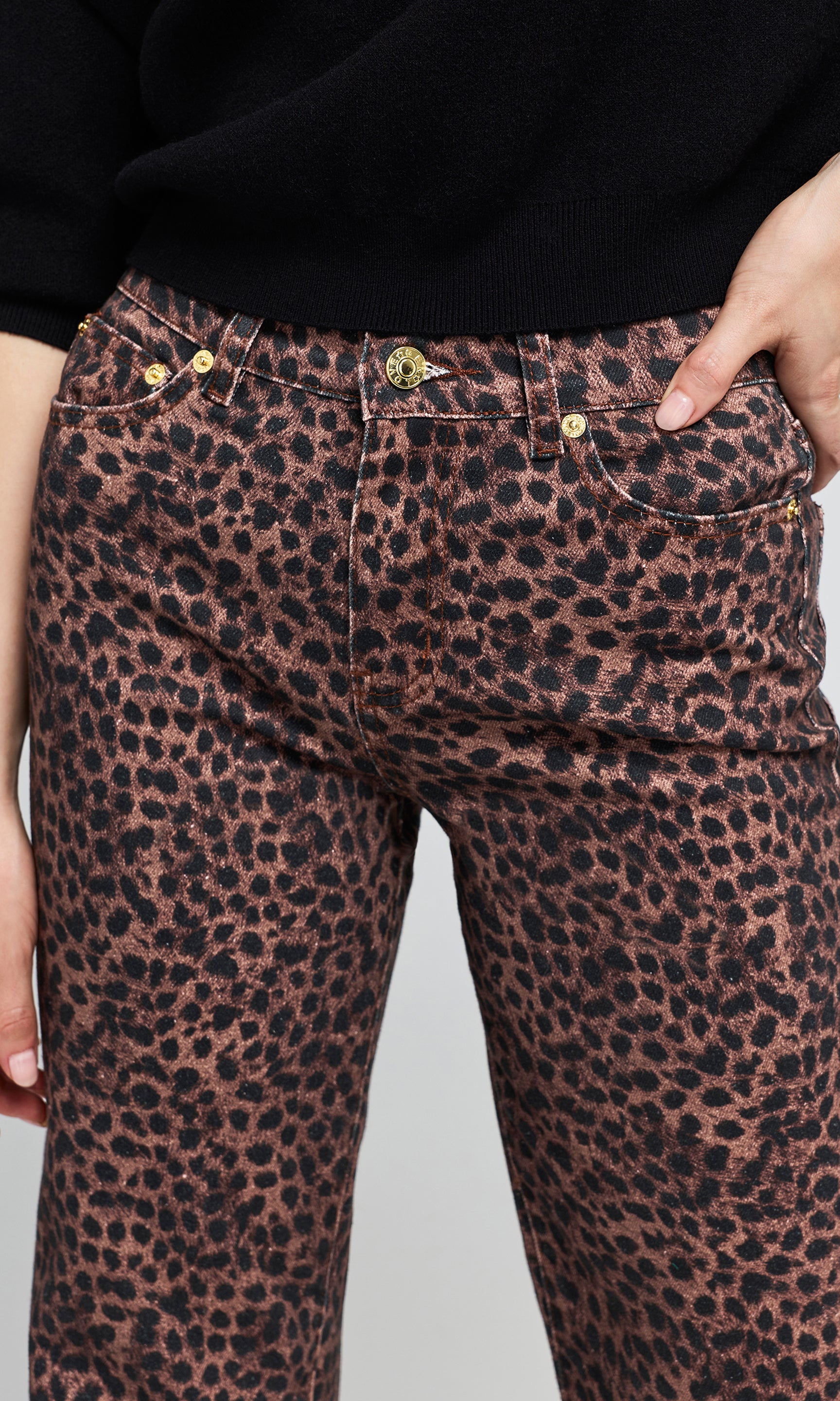 Close-up of a leopard-print jeans with a black top, showing the front waistband, gold-tone hardware.