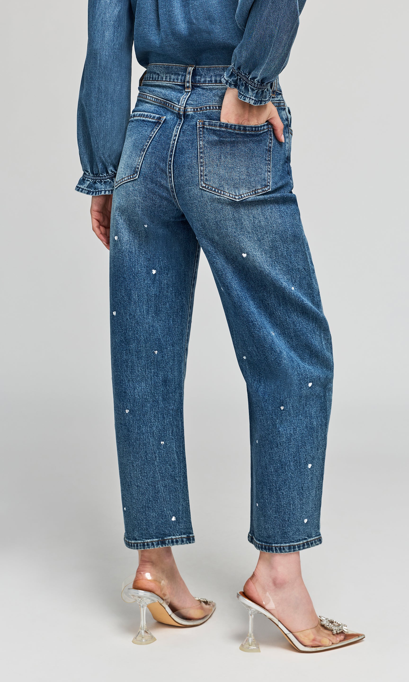 Back view of model wearing blue denim jeans with small heart crystal embellishments down the front, styled with a matching denim shirt.