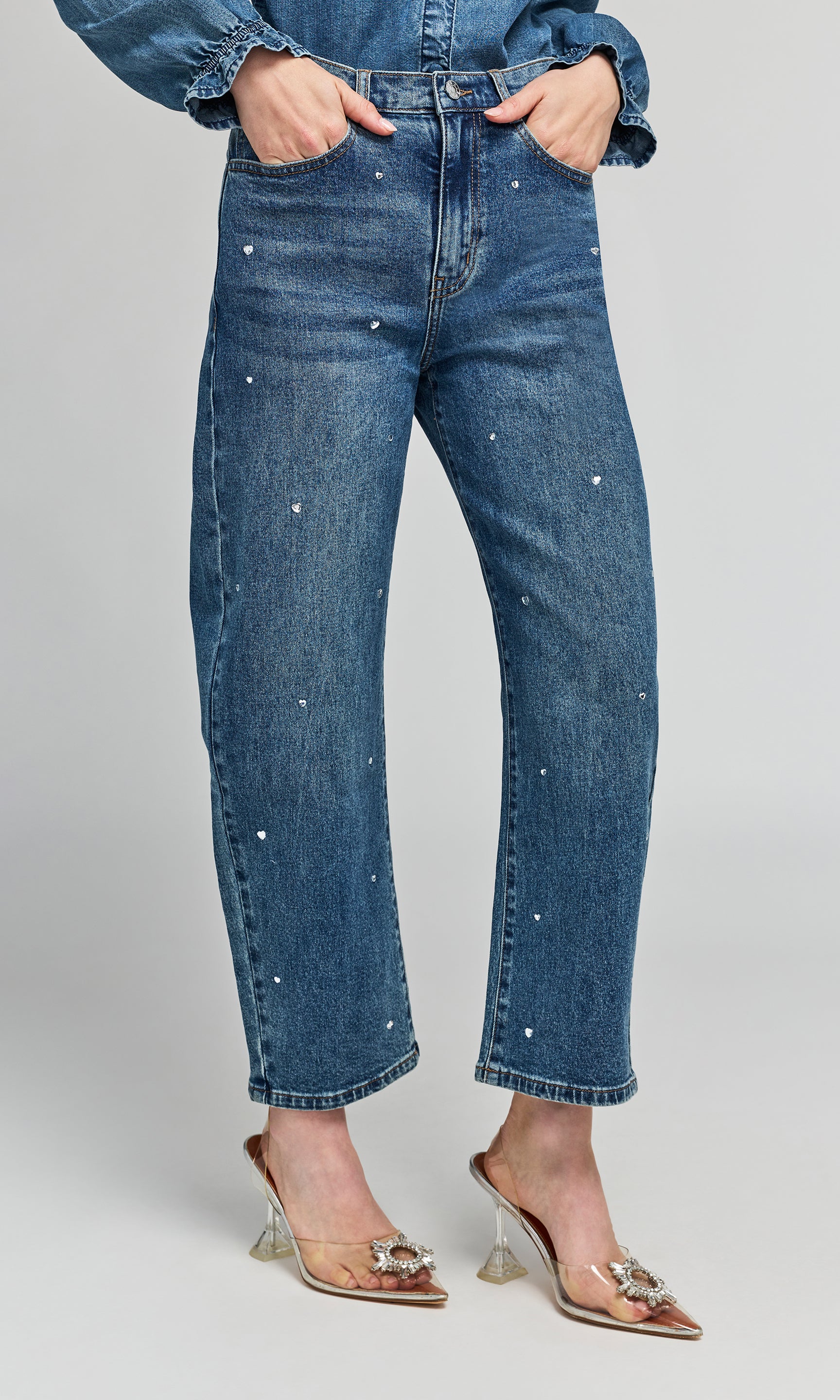 Side view of model wearing blue denim jeans with small heart crystal embellishments down the front, styled with a matching denim shirt.